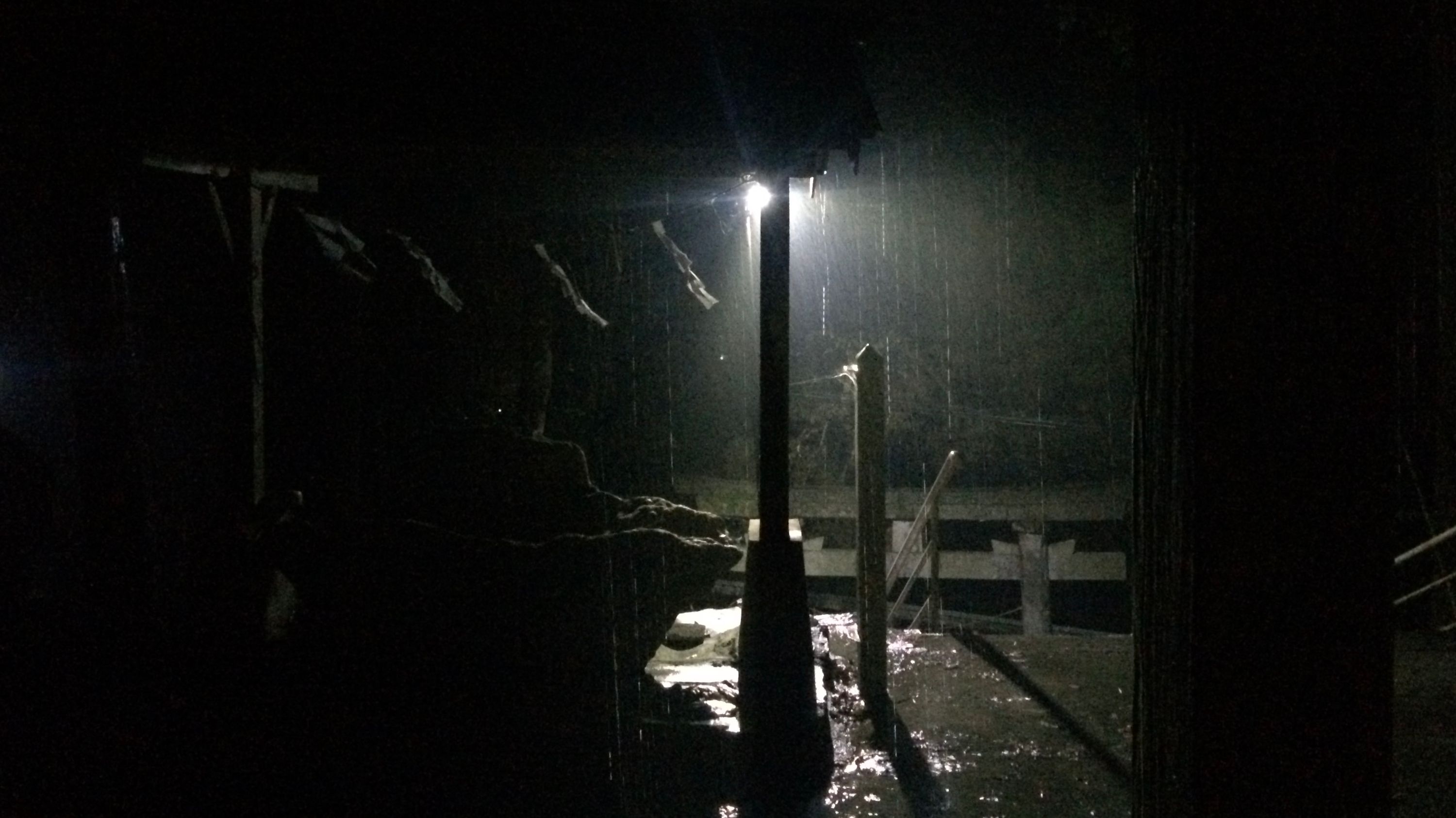 Heavy rain falling at night as seen from the porch of a shrine, with a harsh light shining straight into the camera.
