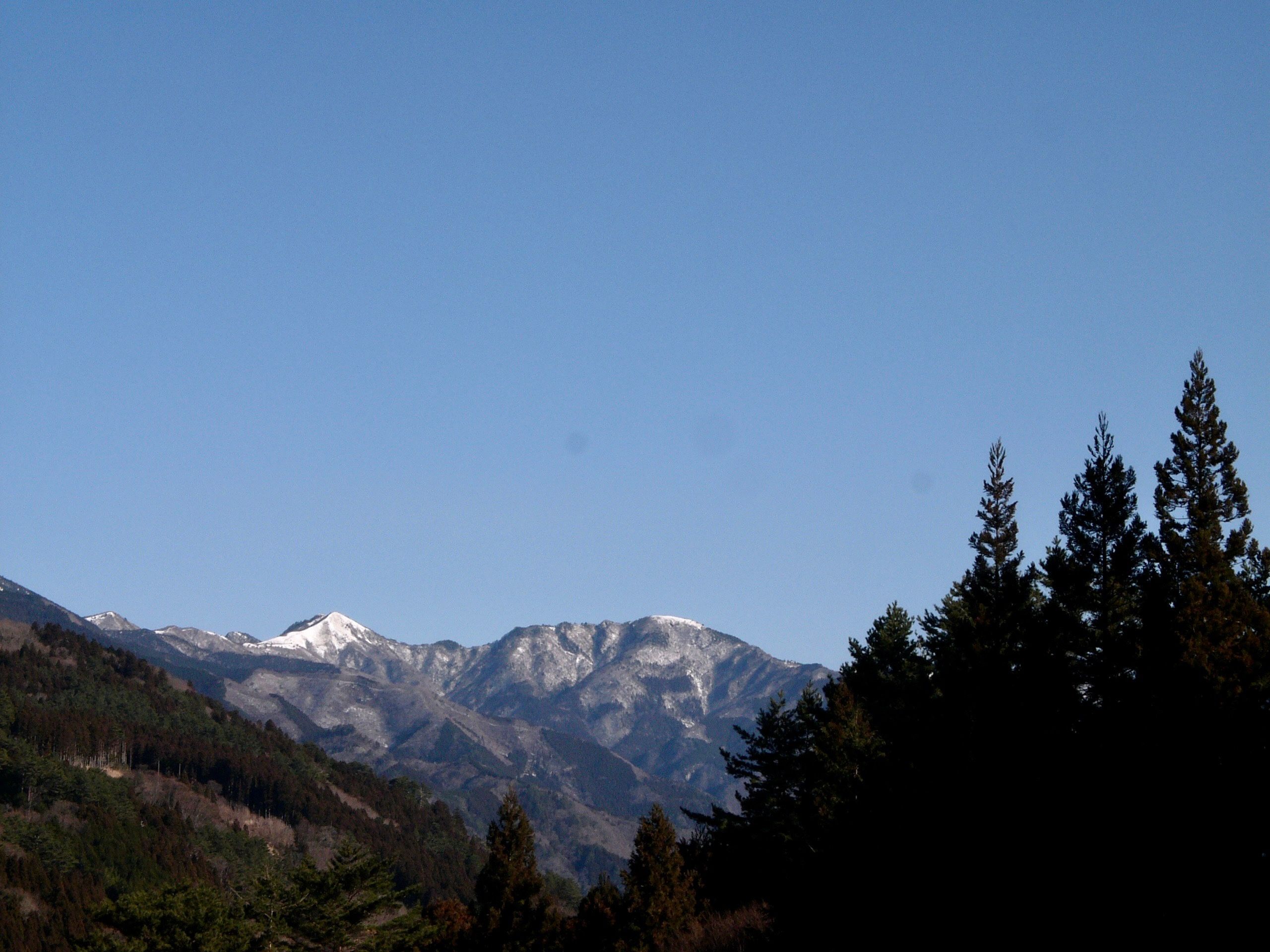 A panorama of forested mountains on a clear winter day, with a snowy pyramid, Mount Tenguzuka, on the horizon.