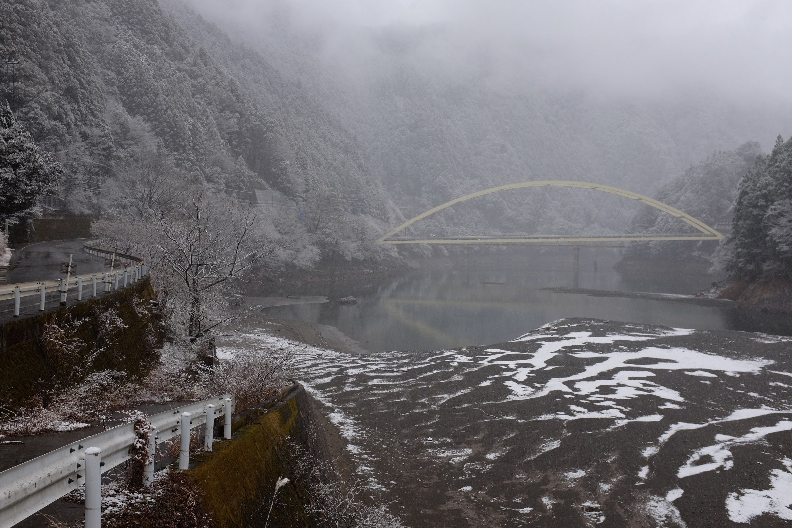 A yellow bridge straddles a river in a steep valley where the trees are all covered in fresh snow.