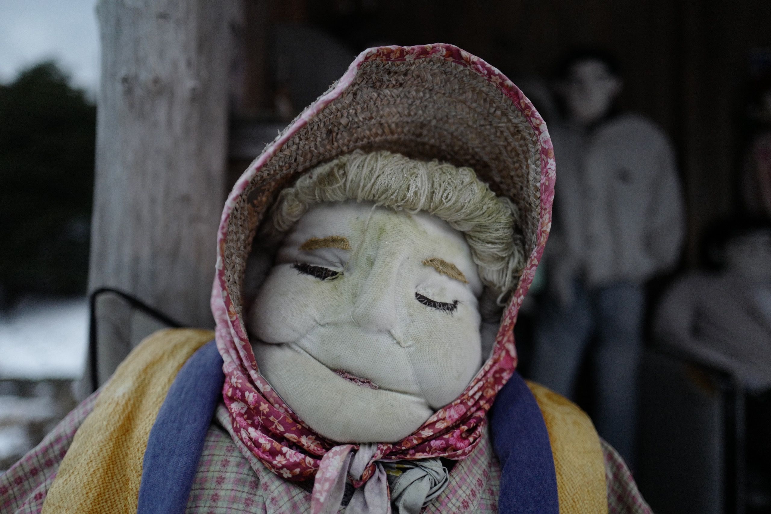 Closeup of another similar doll, this one with the features of an older woman wearing a straw cap and a scarf.