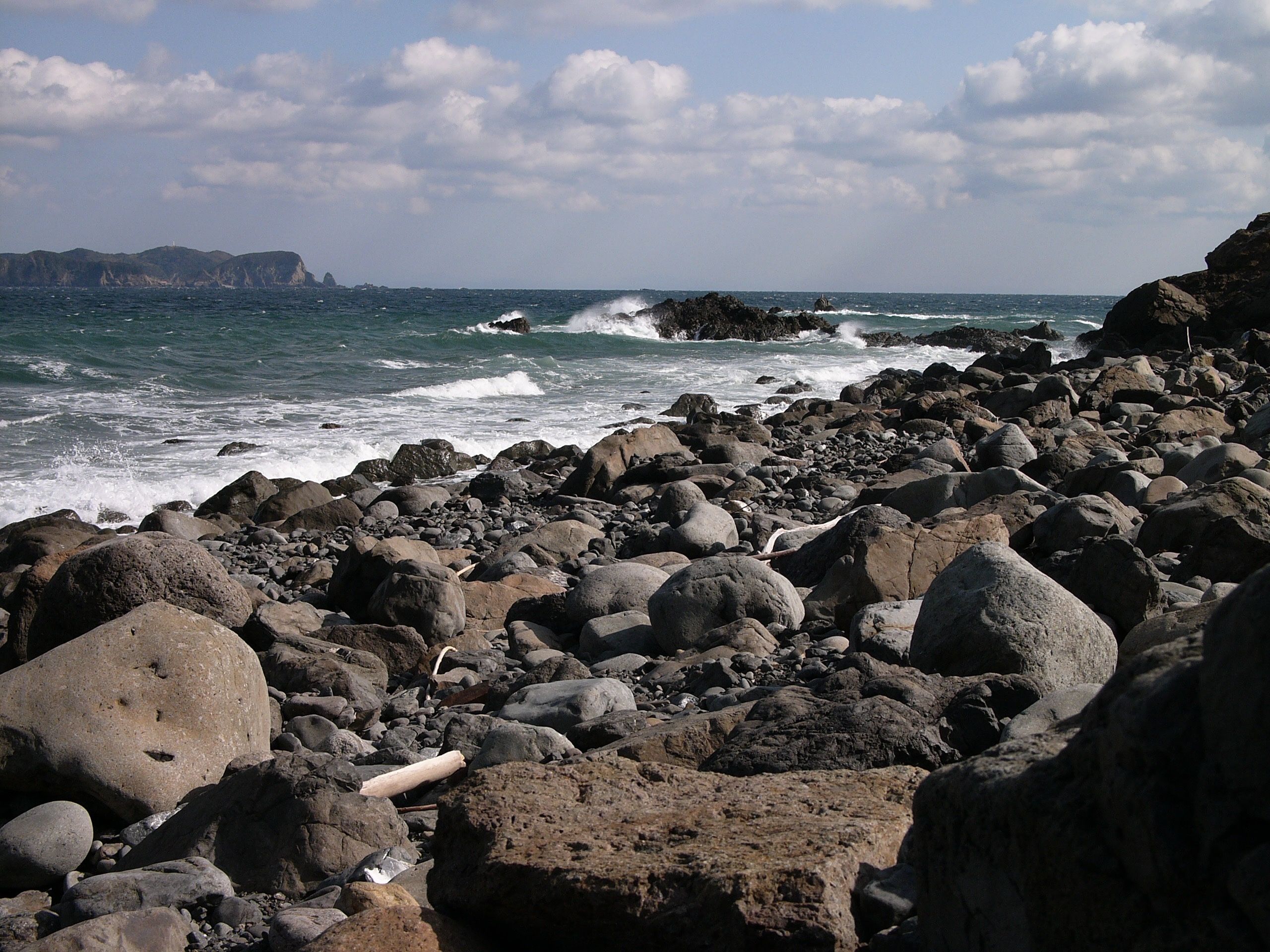 A cold-looking, choppy sea from a rocky beach with a small island on the horizon.