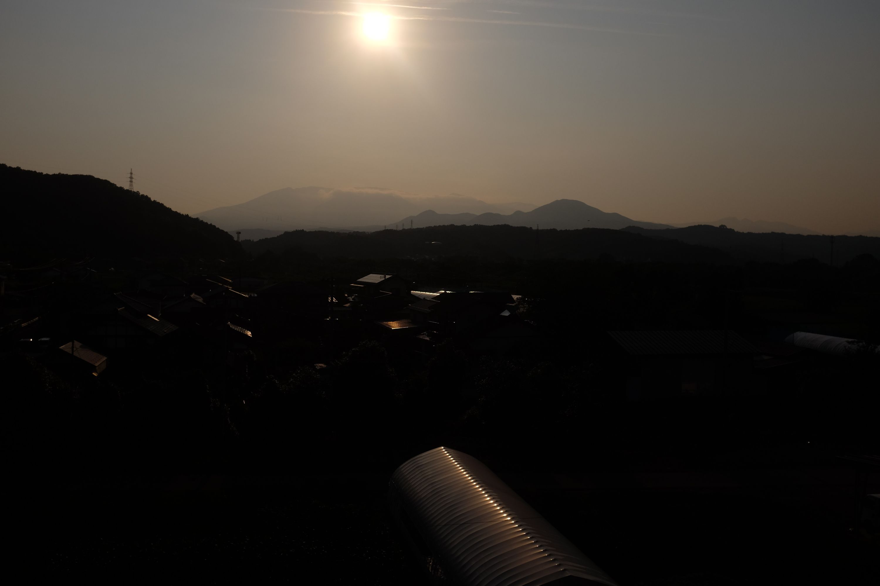 Looking out against the late afternoon sun over a small town, with a large, broad mountain on the horizon.