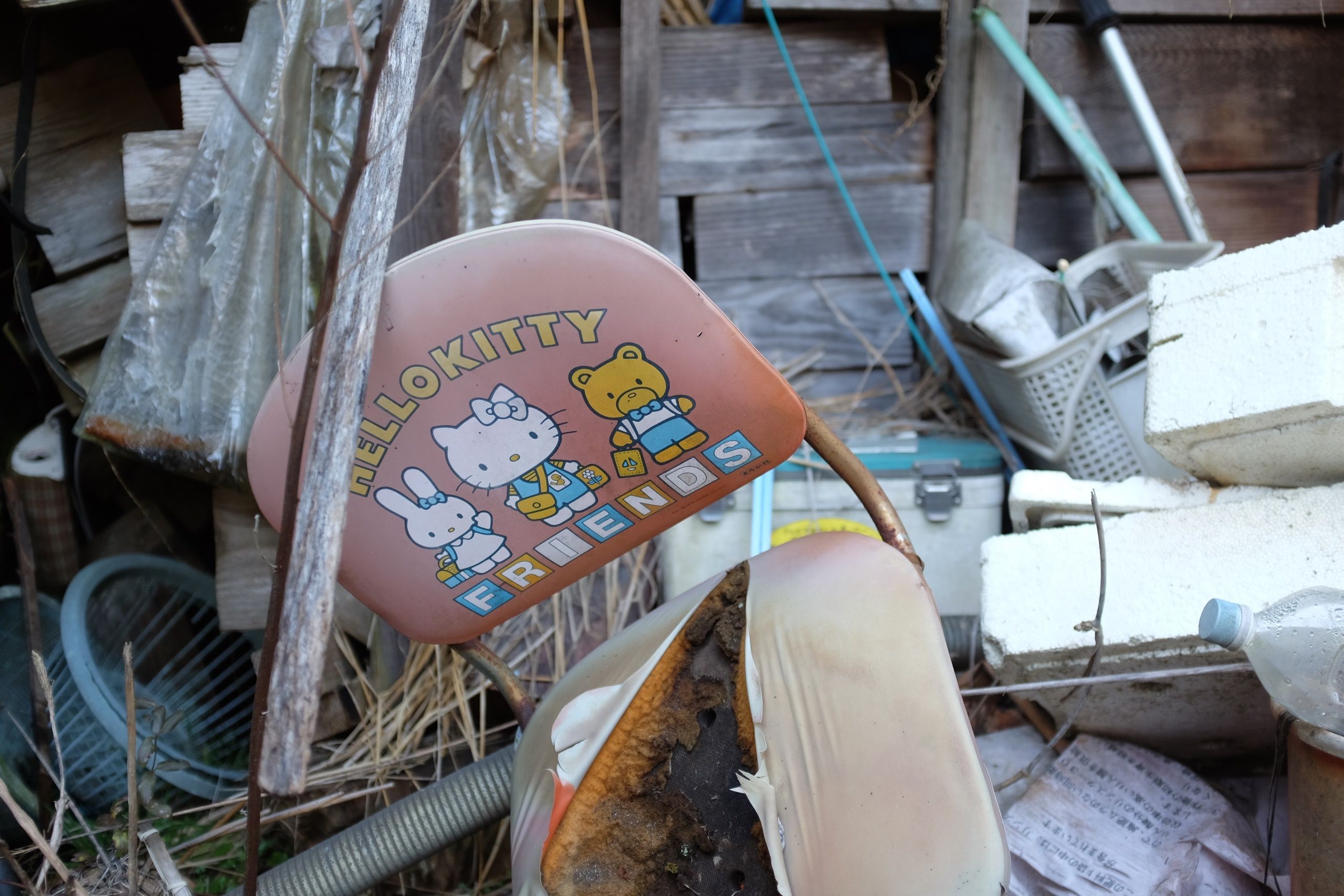 A half-burned chair that says Hello Kitty Friends, showing Hello Kitty and her friends, in a trash-filled shed.