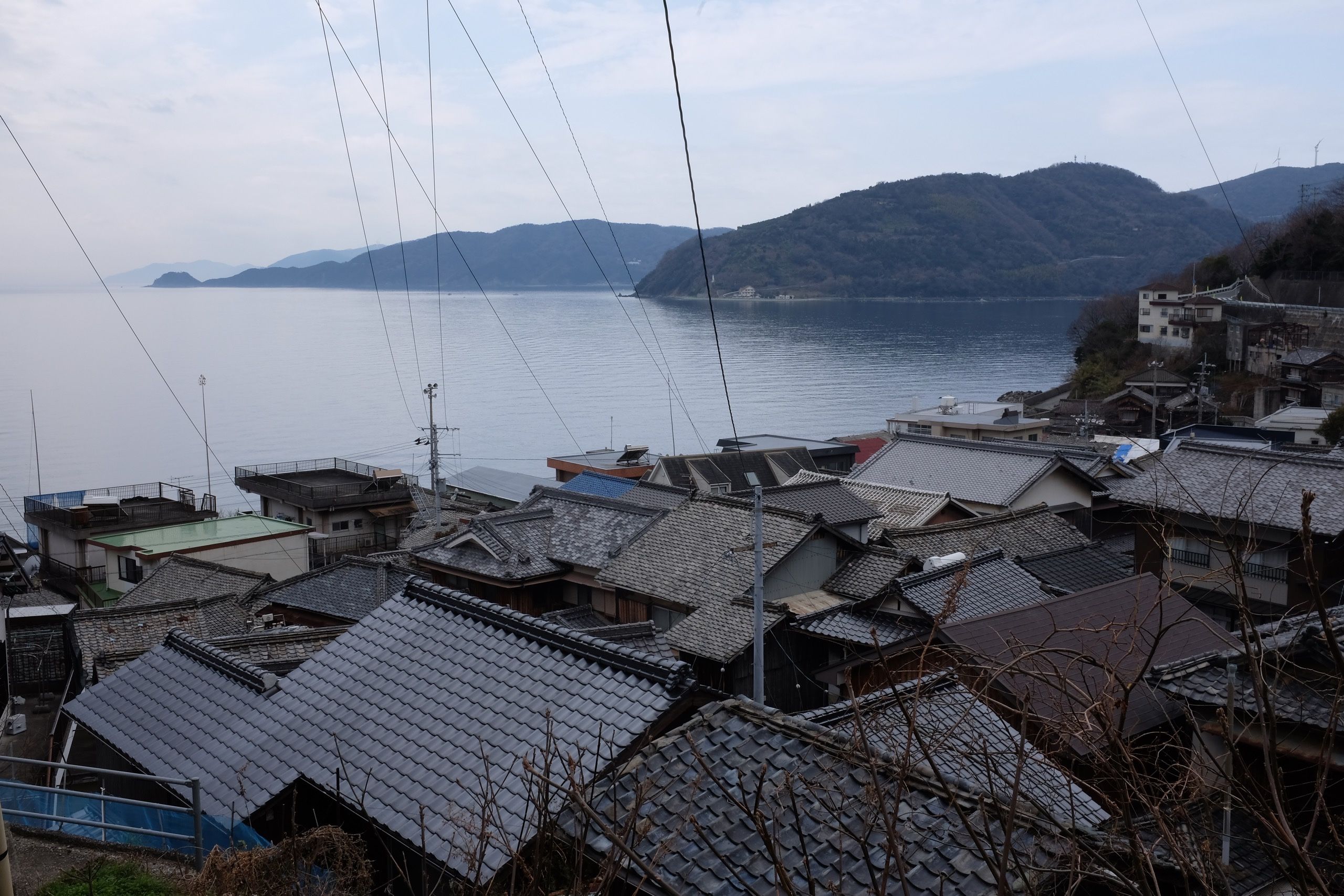 A very tight cluster of houses form a fishing village in a bay, with power lines descending almost vertically from above.
