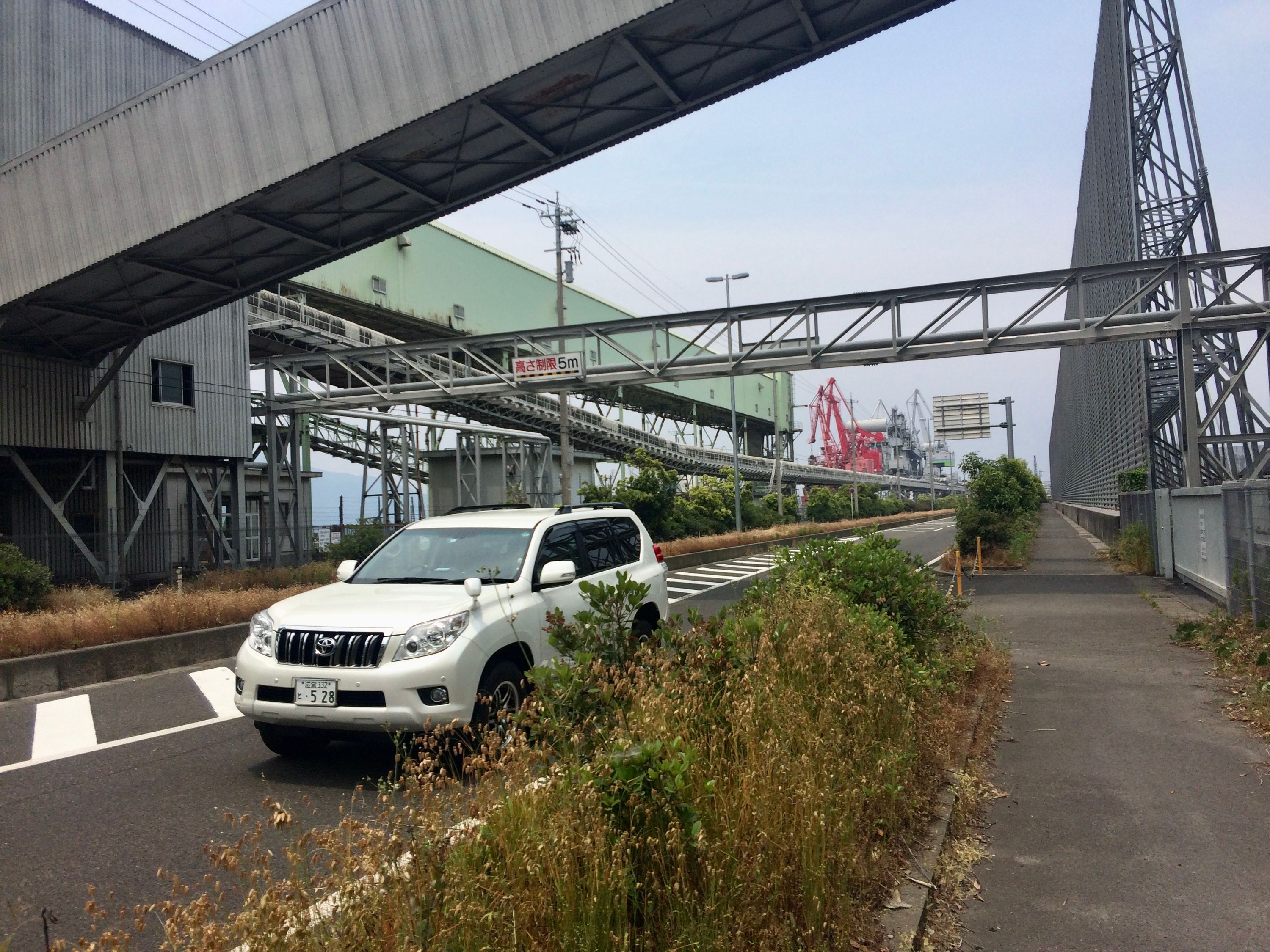 A white SUV drives on a road which runs across a cement factory.