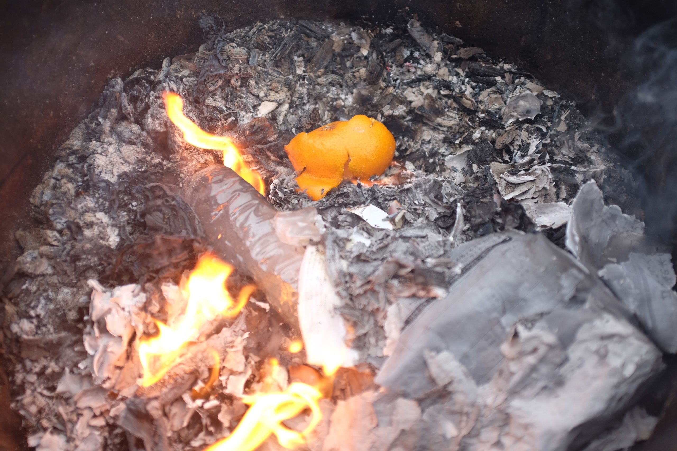 Orange peels thrown on a trash fire in a metal drum.