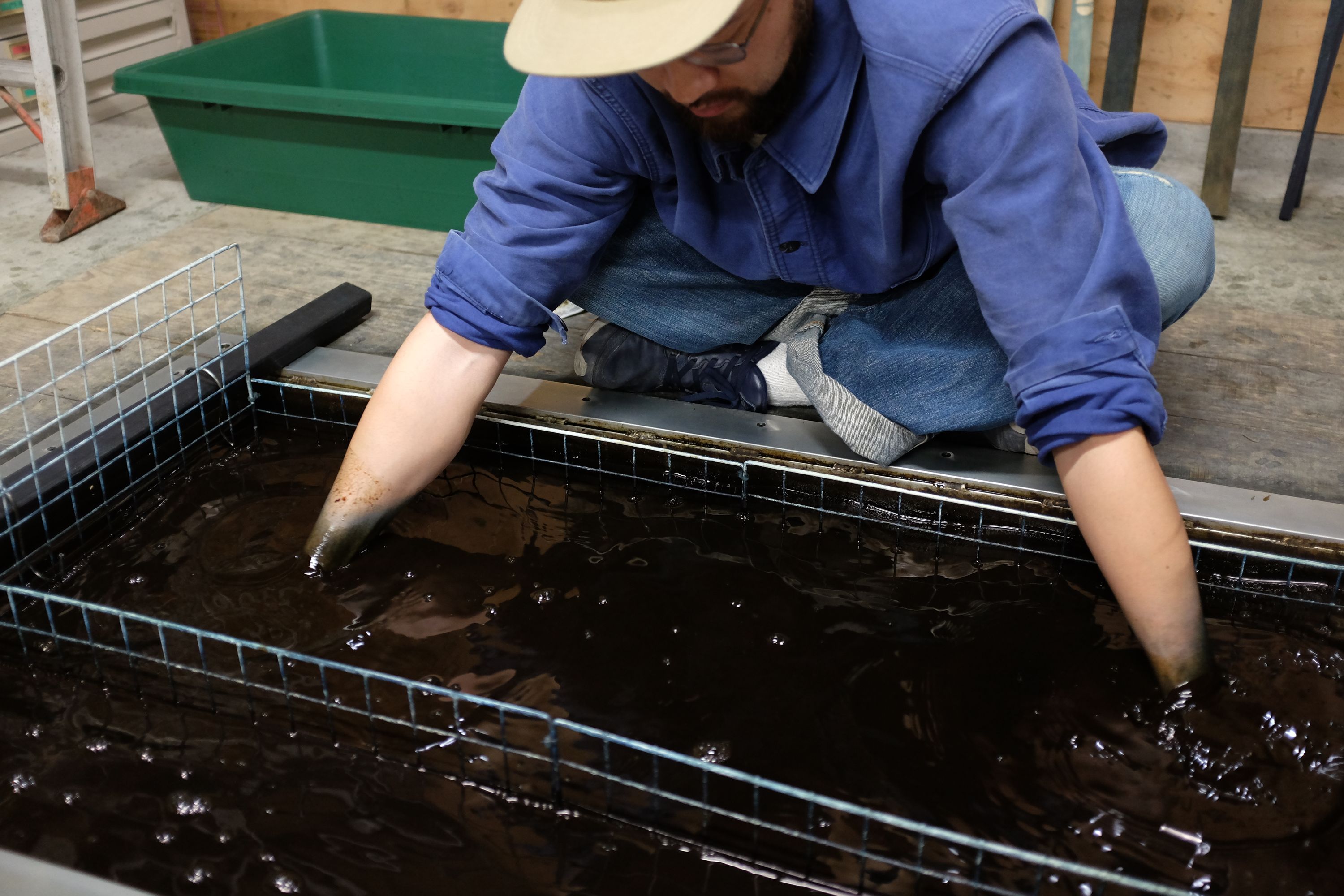 A Japanese man dyes a shirt in a vat of indigo.