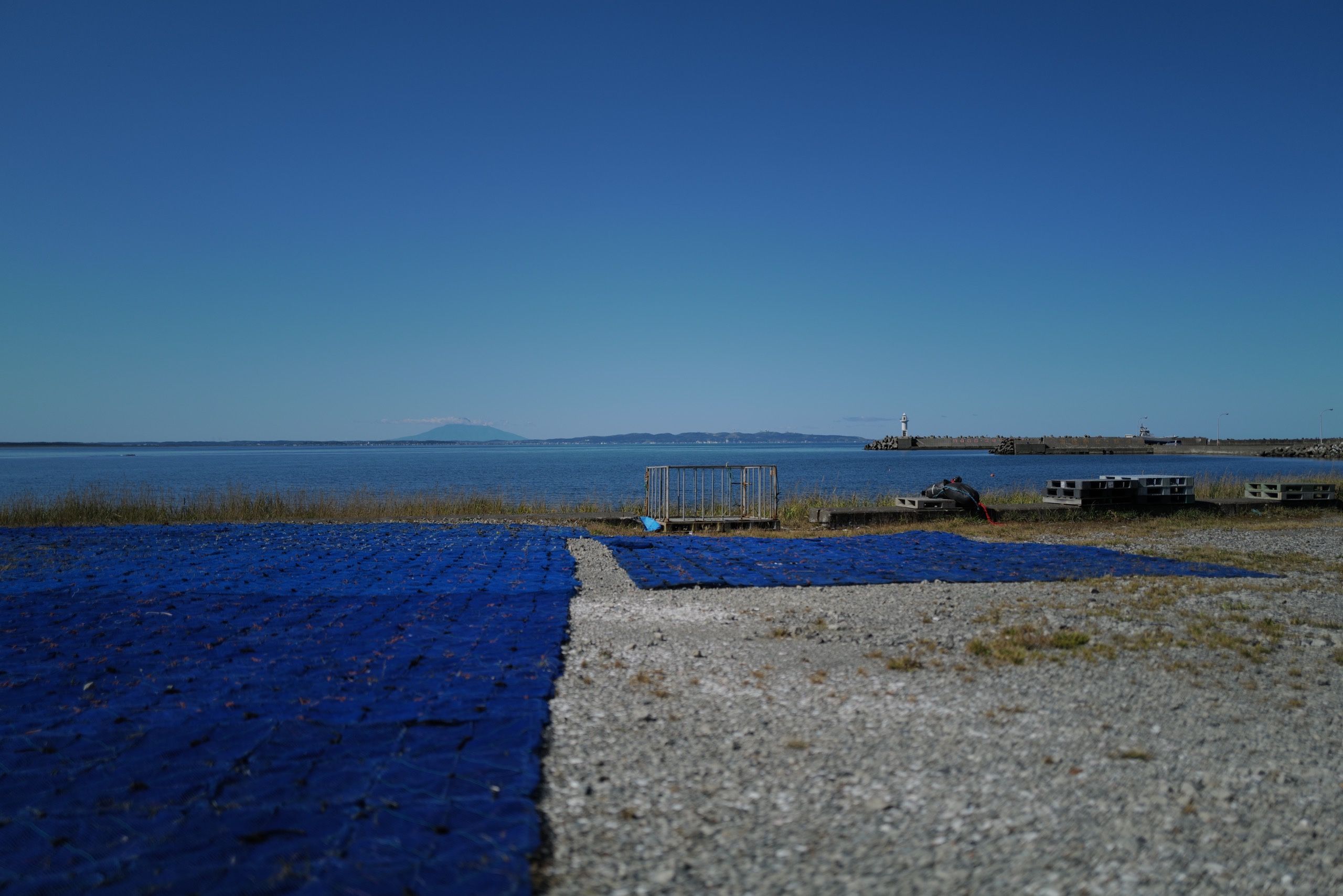 Behind a bay and a deep blue netting laid out to dry, a volcano, Rishiri, is seen on the horizon