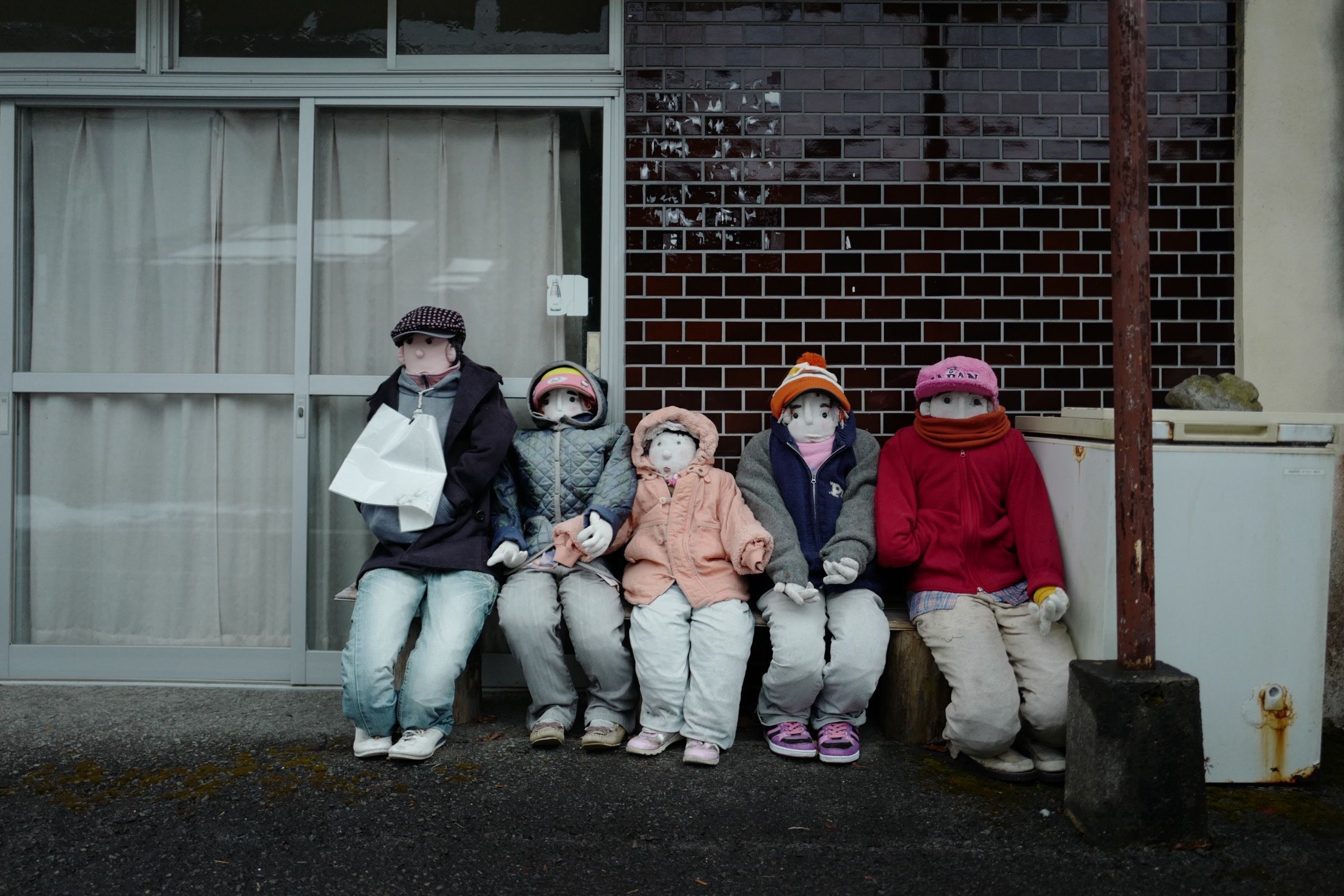 A row of five human-sized dolls sit in front of a house.