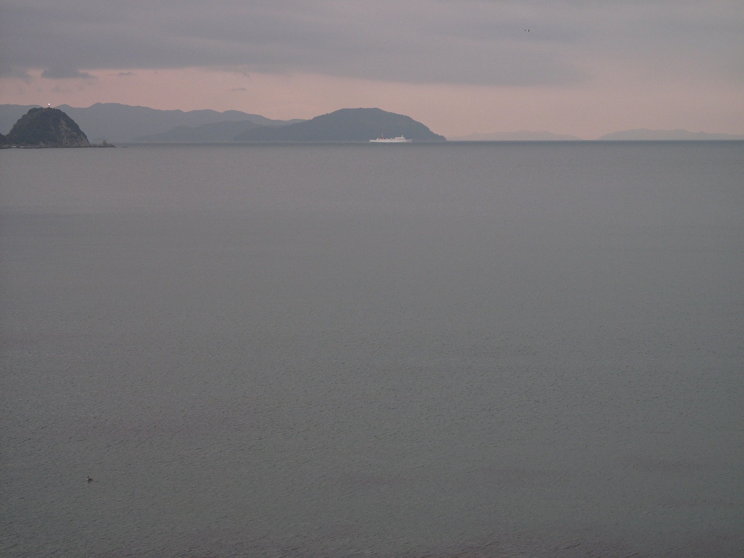 A pink and lavender and grey seascape with small islands and a white ferry in the distance.