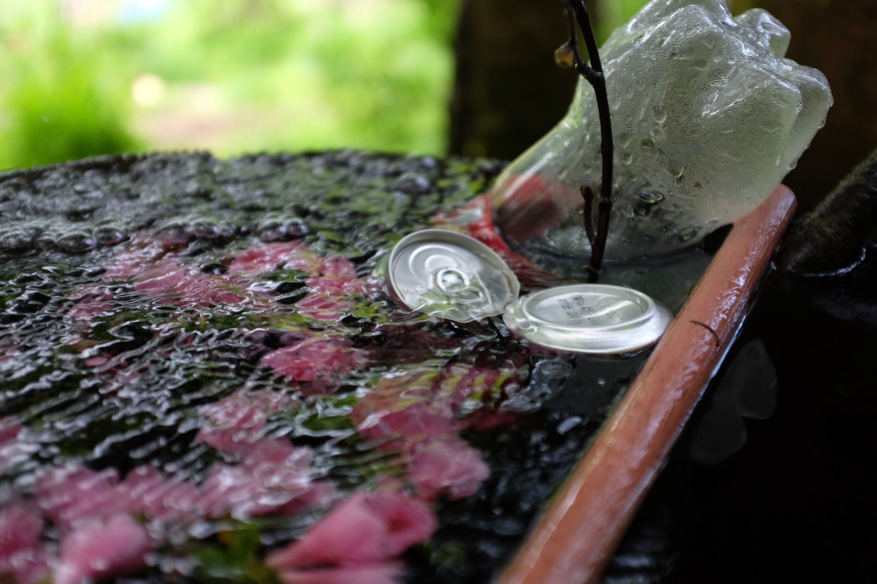 Two beverage cans and a plastic bottle are placed to cool in a bucket of spring water.