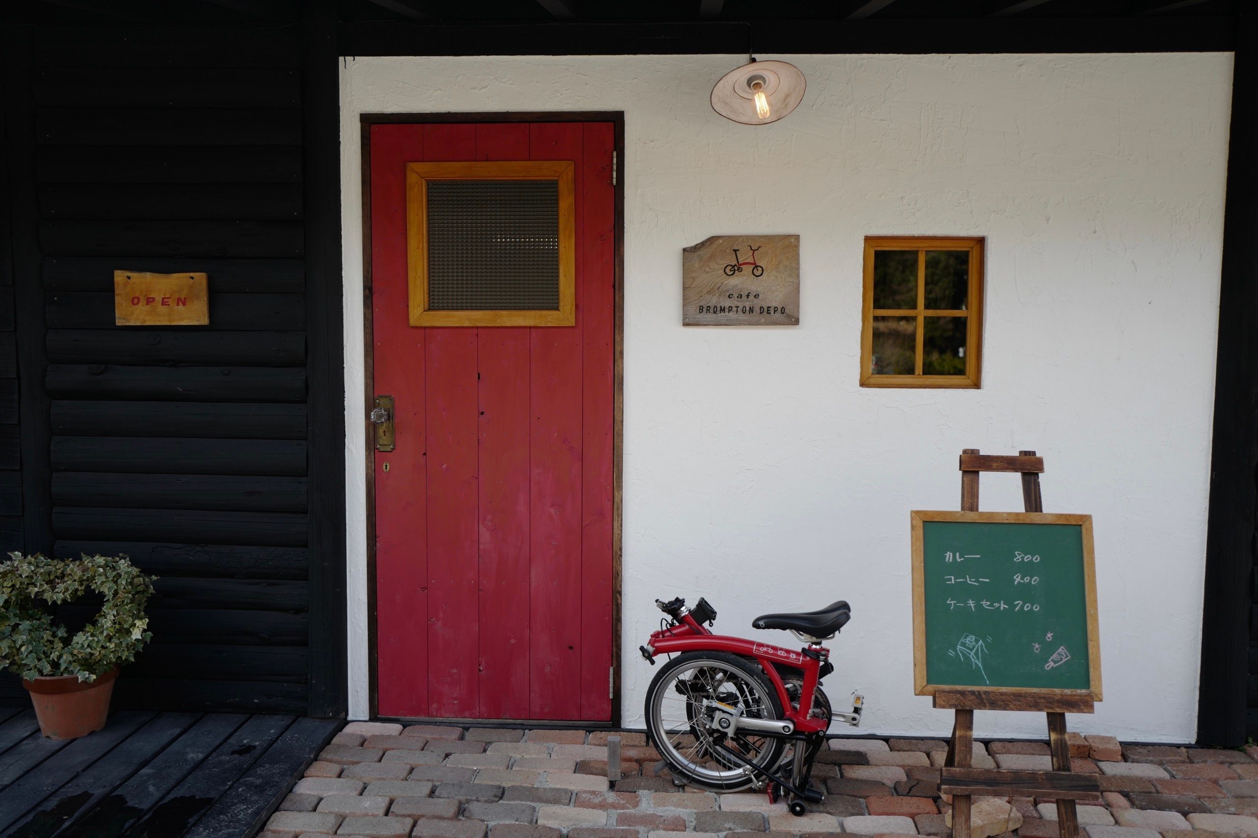 A red Brompton folding bicycle in front of a cafe that sells curry and coffee.