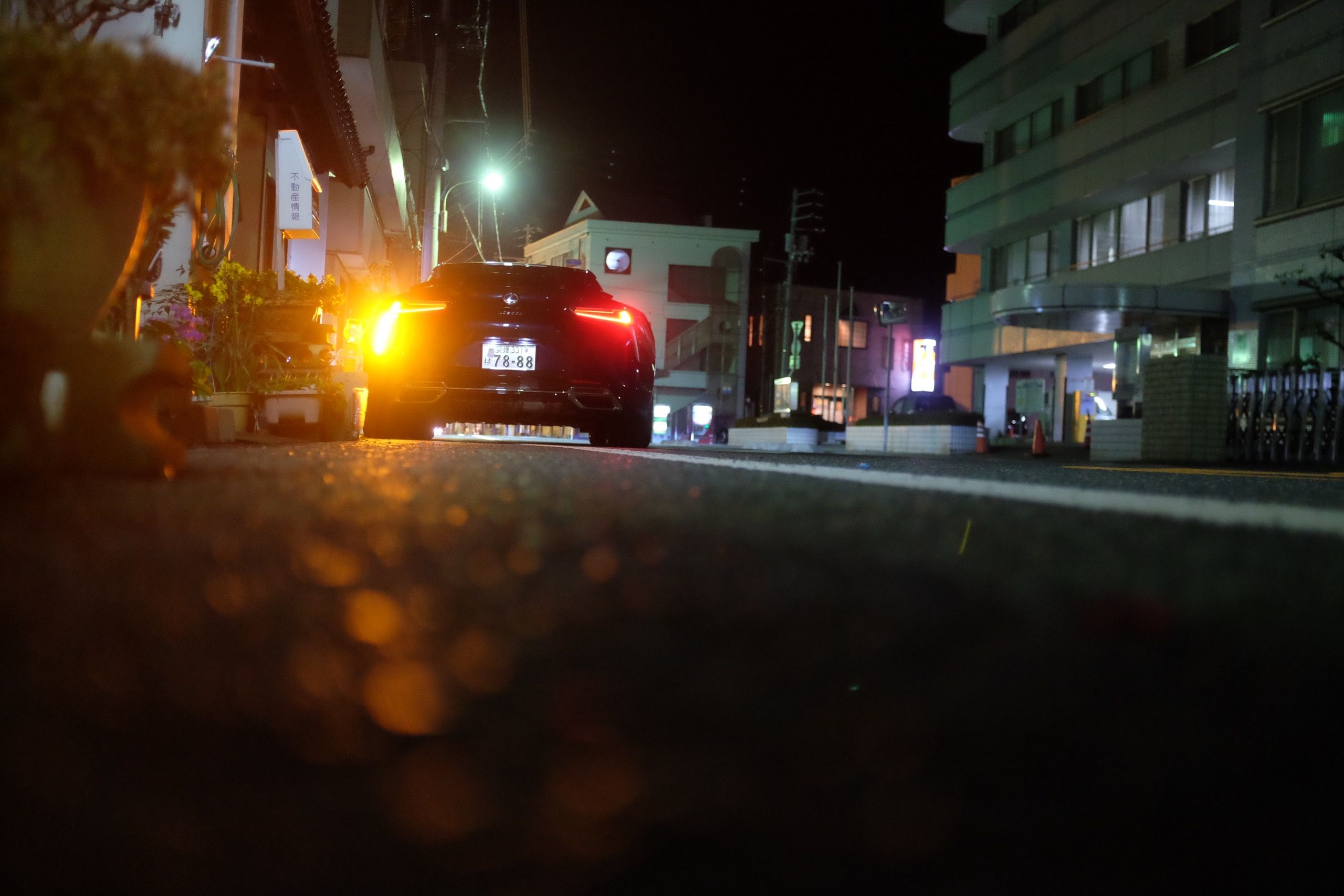 A frog’s eye view of a Lexus LS500 sports car stands parked on a street with its brake lights on and reflected on the asphalt.