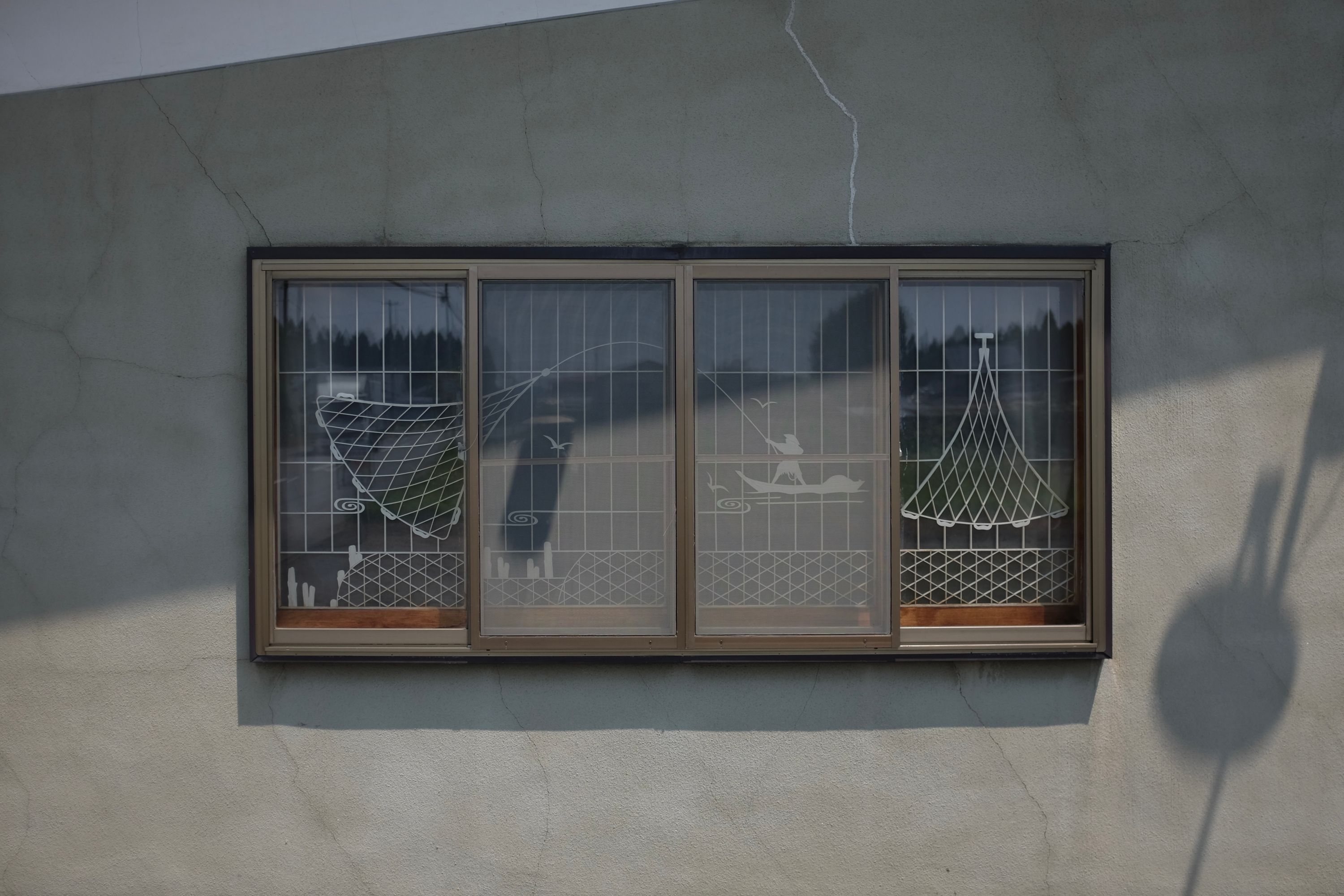 The window of a house features a line drawing of a person fishing with a net from a small boat.