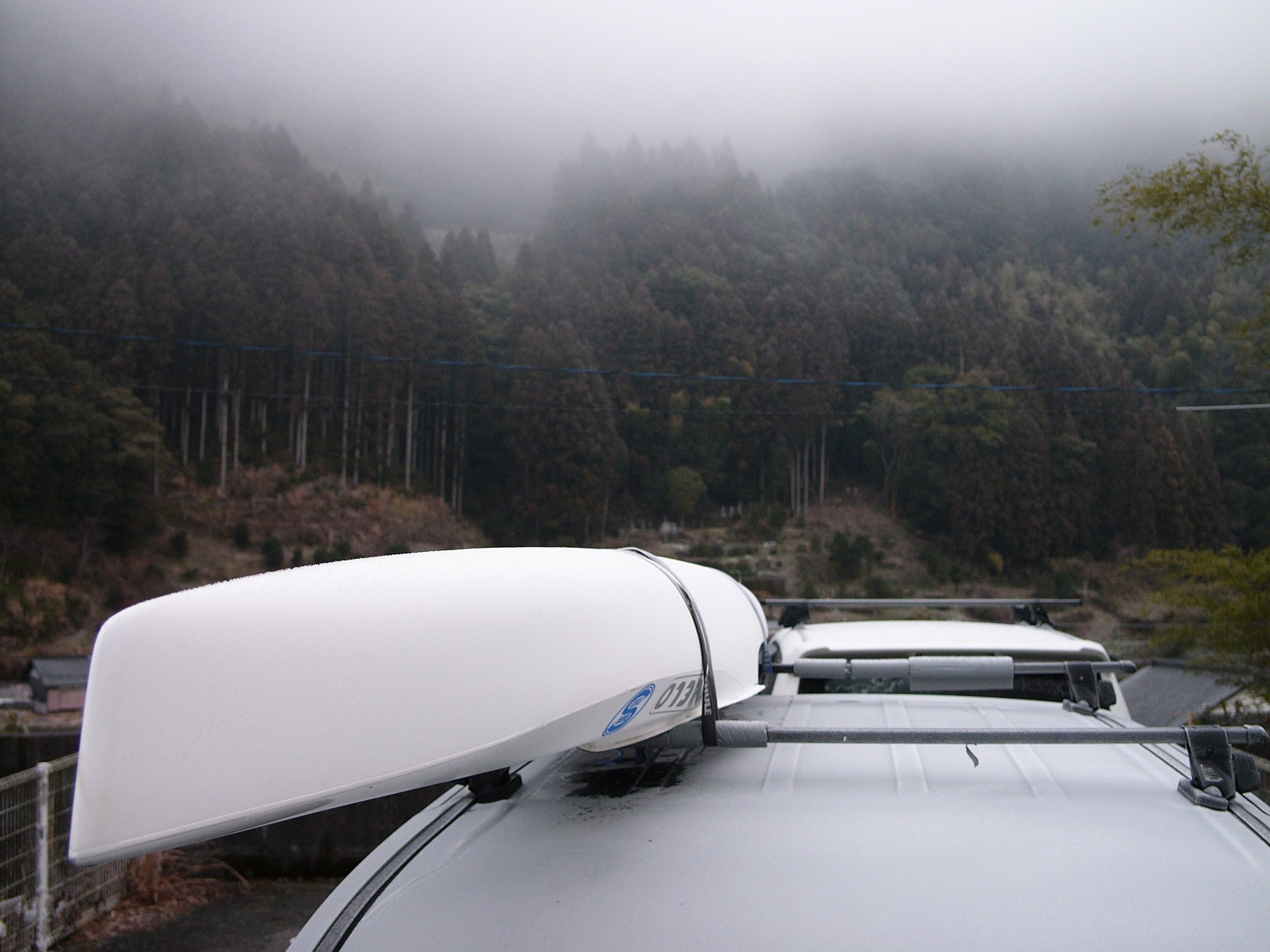 A white racing kayak on the roof of a vehicle.