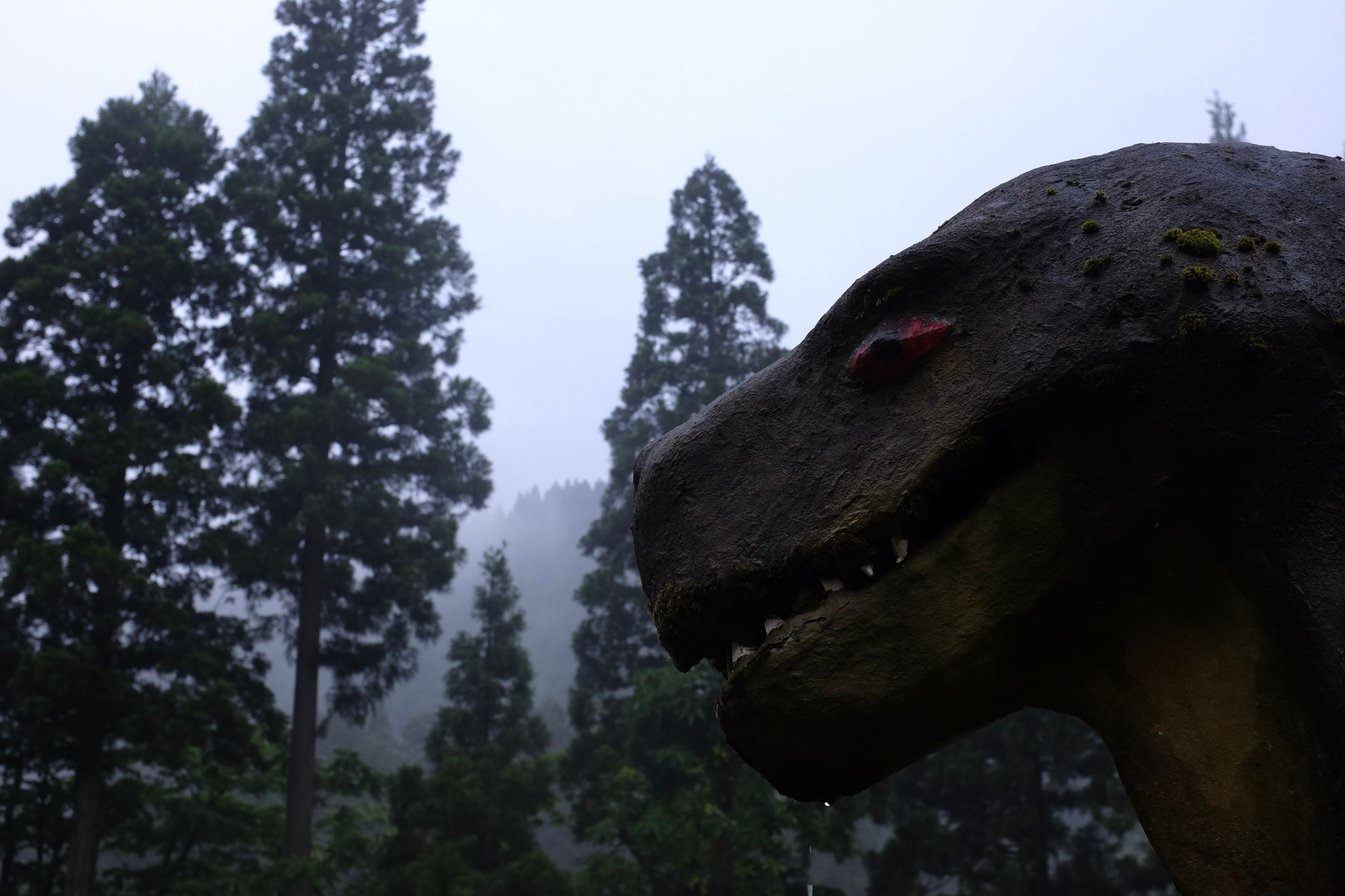 Head of a theropod dinosaur looking at a foggy forest.