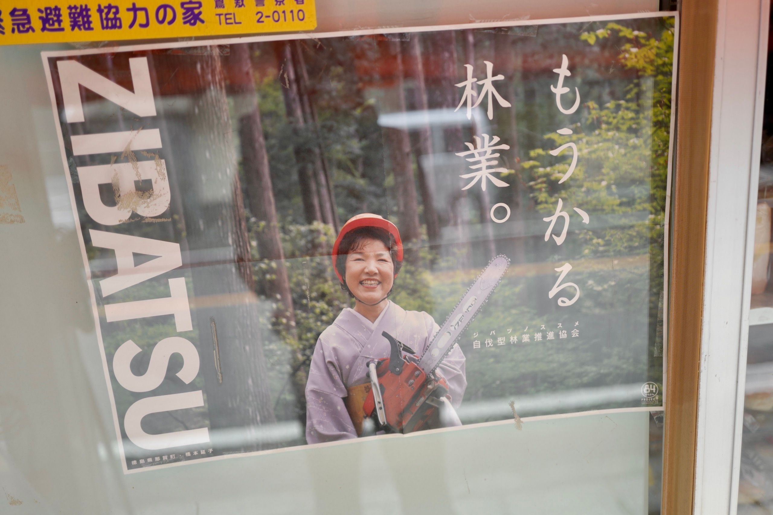 A poster of a smiling woman holding a chainsaw, wearing a red helmet and a pink kimono.