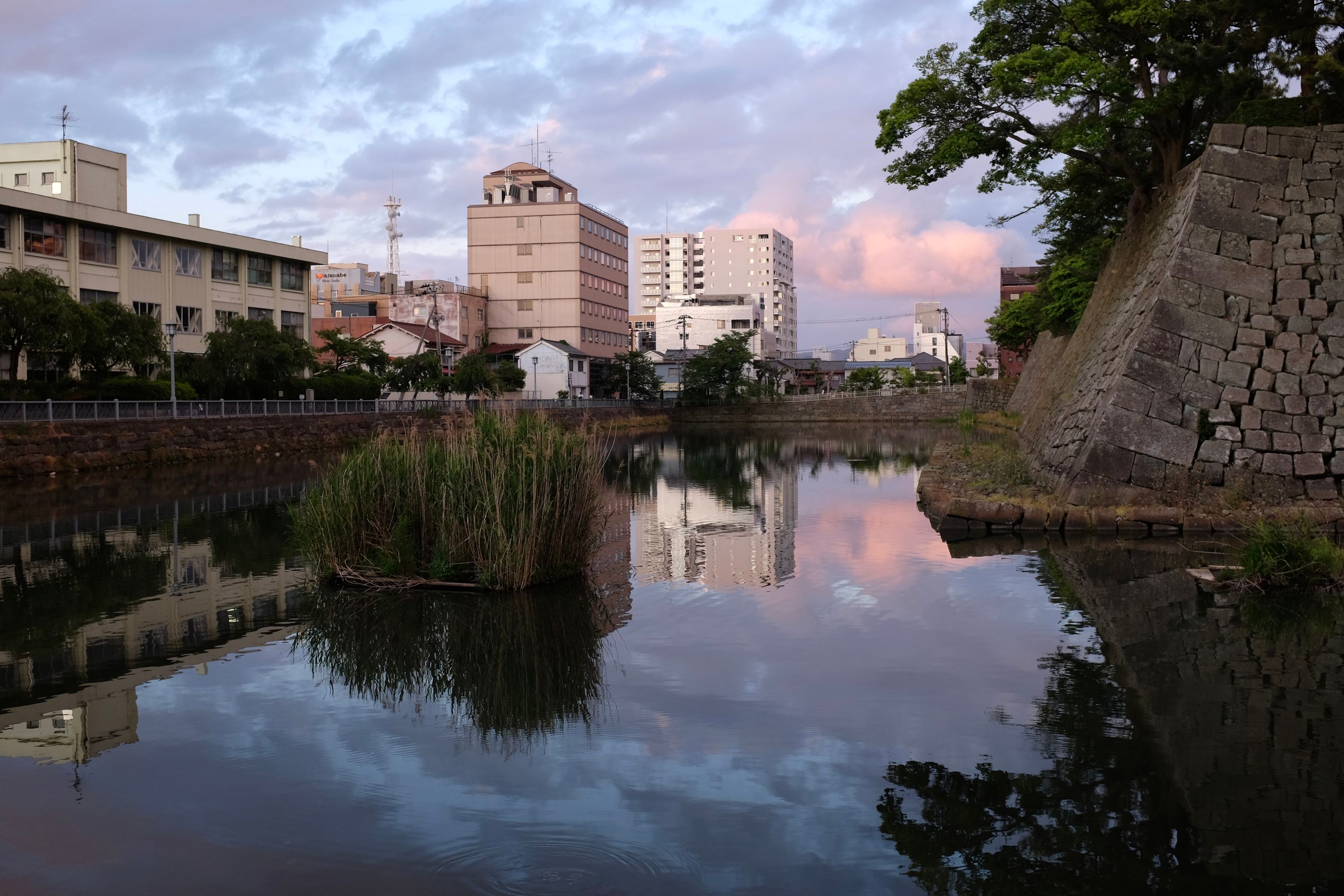 Modern buildings reflected in the water of the moat of a Japanese castle.