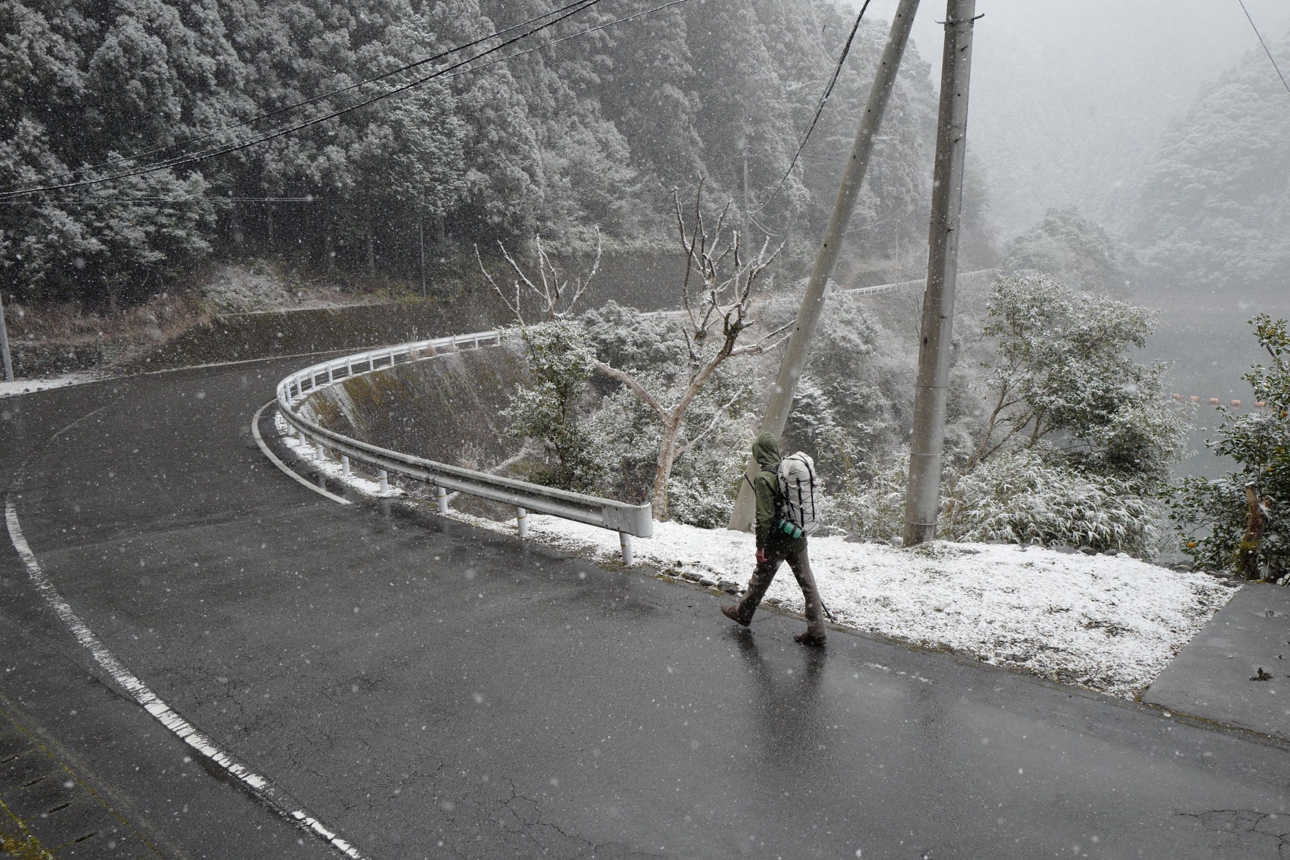 A man with a white rucksack, the author, walks on a road while it is snowing.