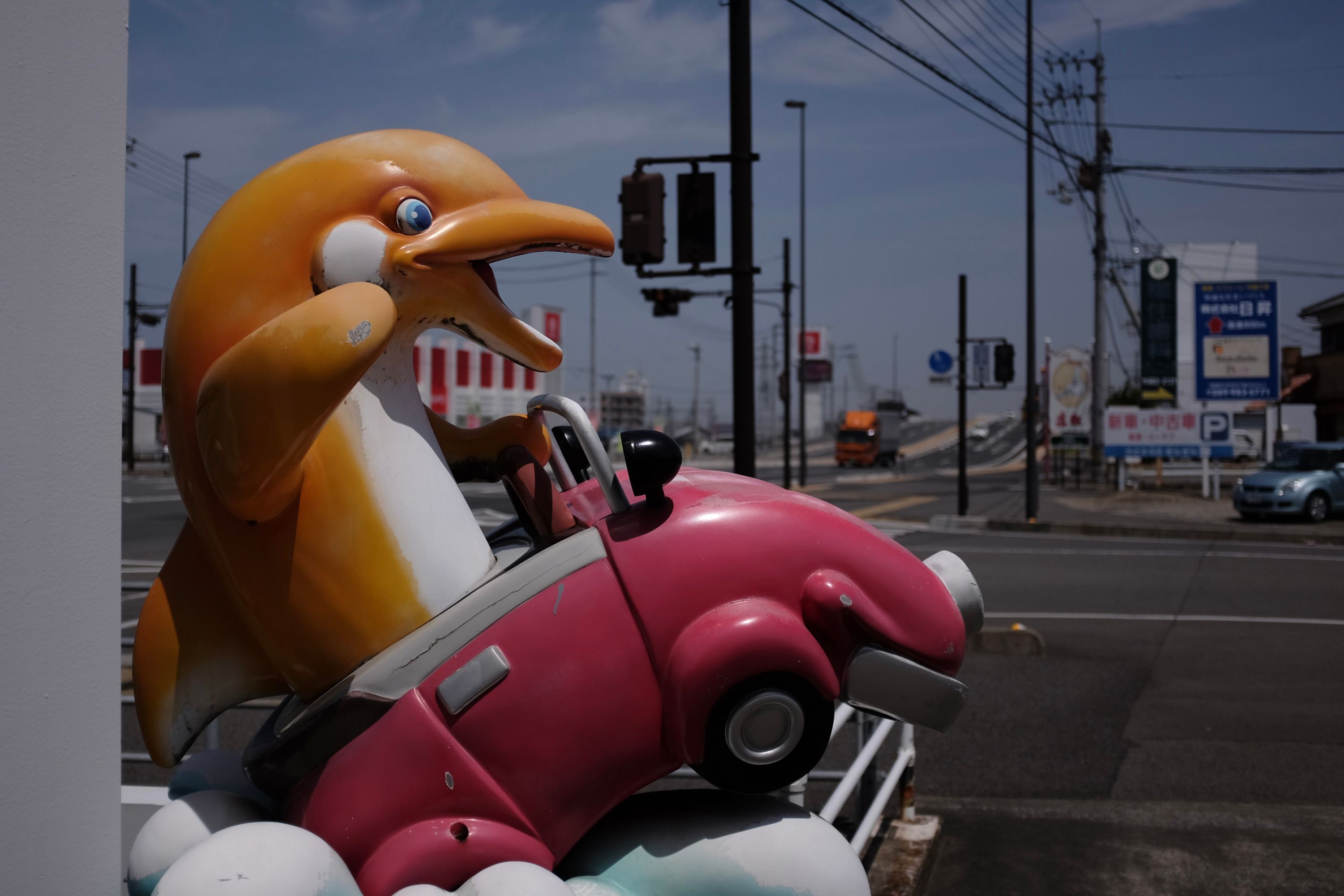 A plastic dolphin drives a red plastic car on the road into Matsuyama.