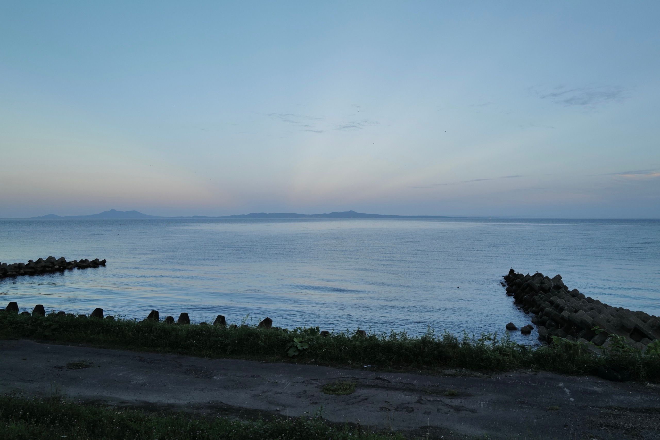 Looking out across the sea at dusk on an island and its chain of volcanoes.