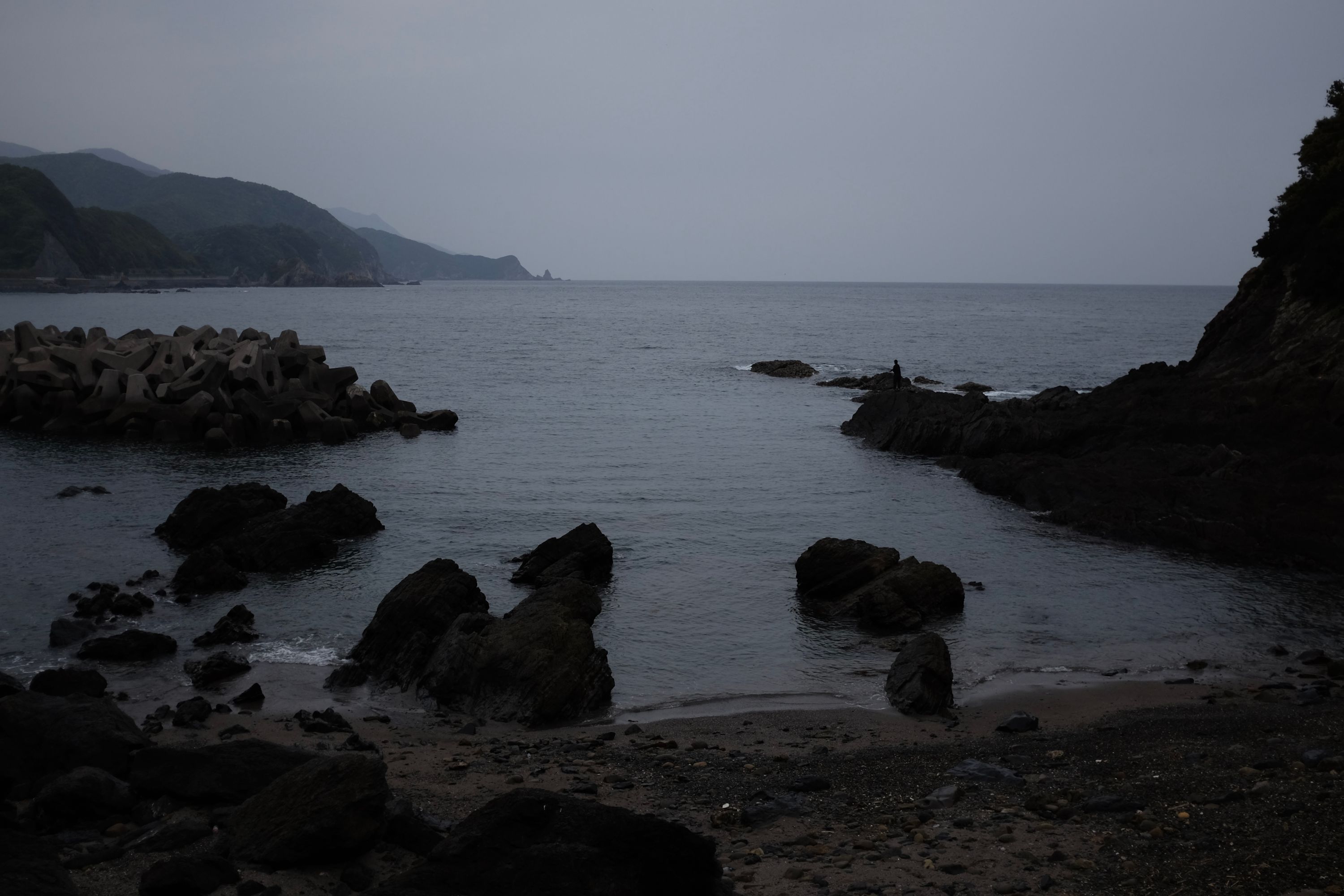 A man fishing in a bay under an overcast sky.