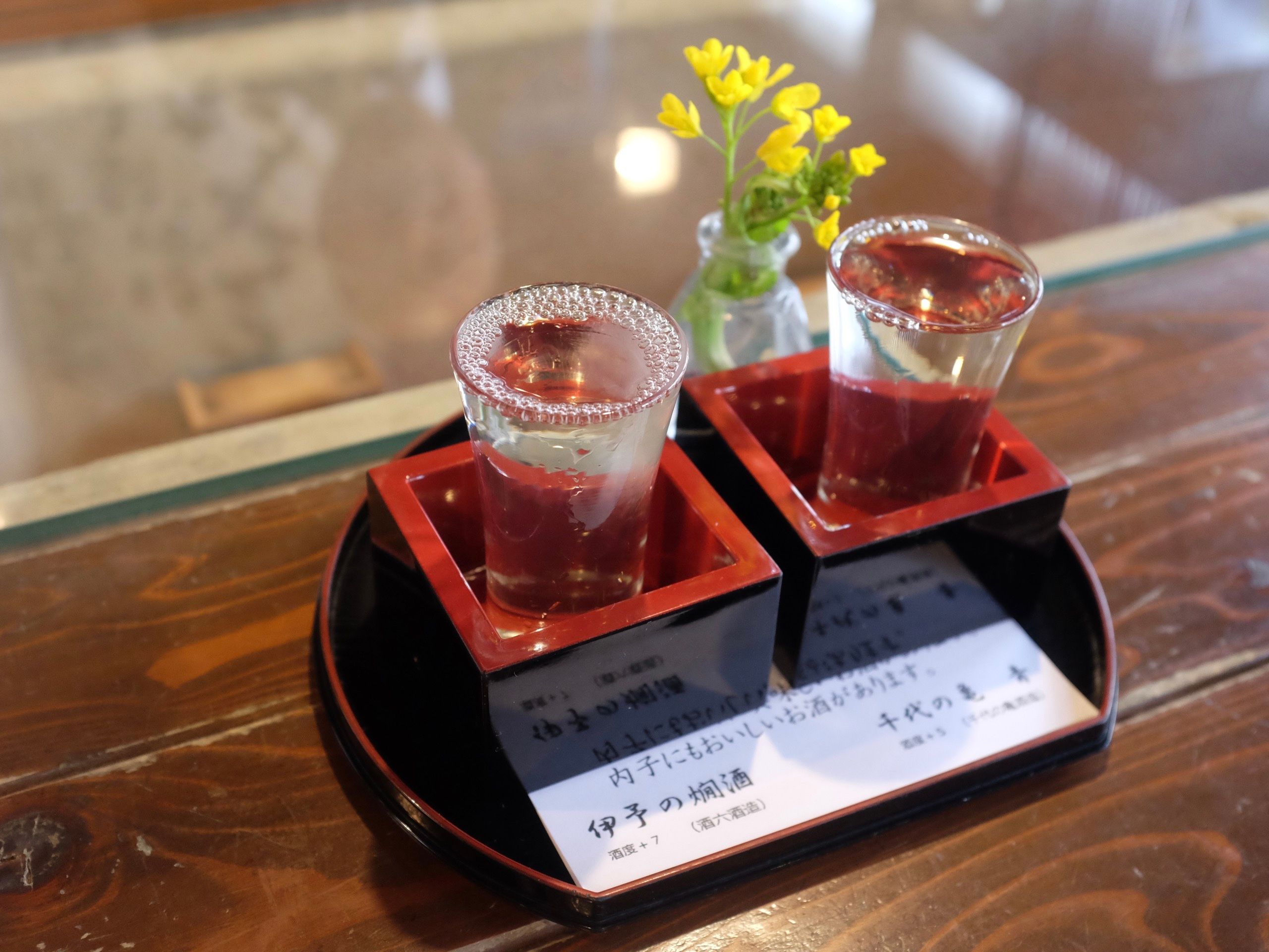 Two glasses of sake served in red and black wooden cups.