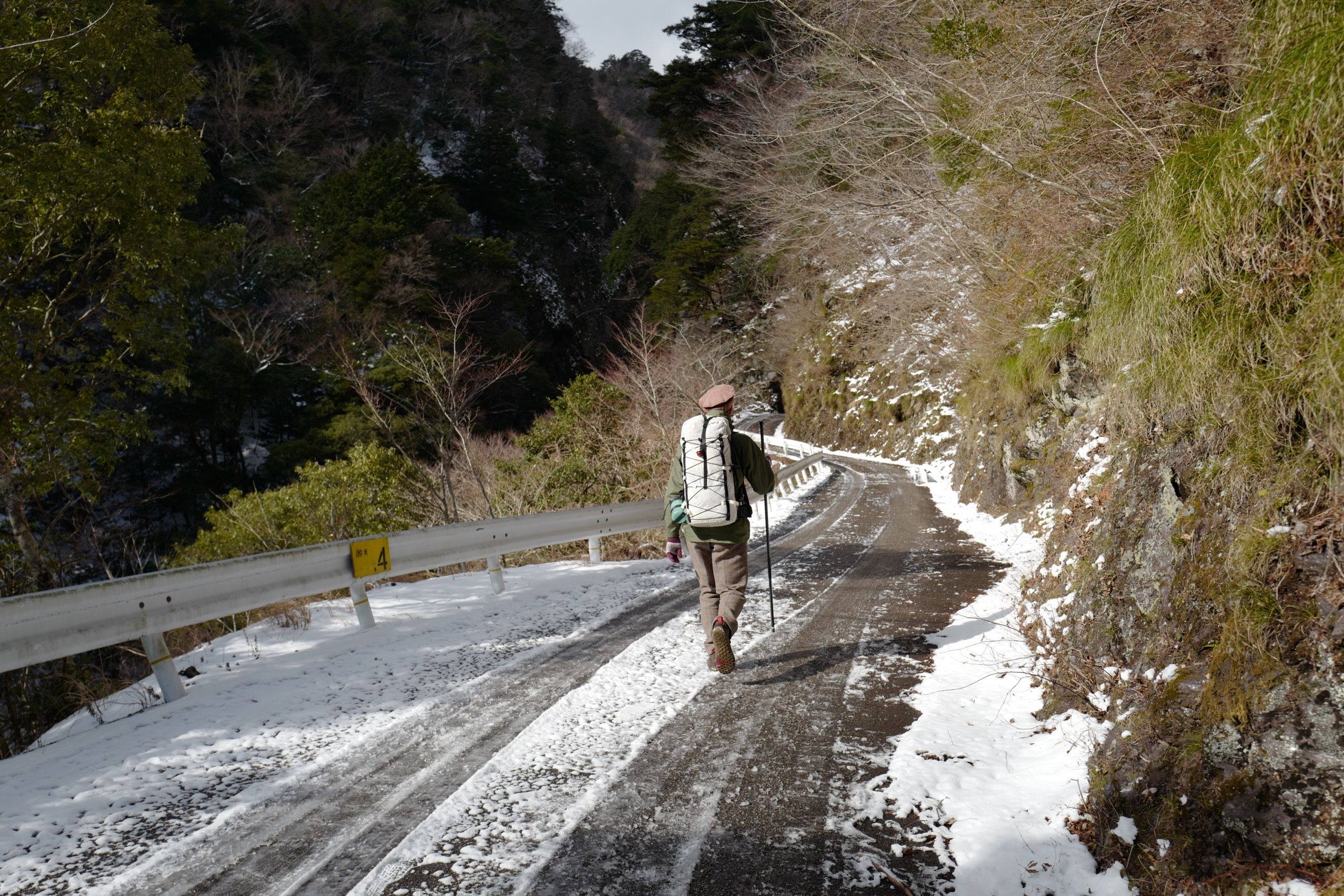 A man carrying a white rucksack, the author, walks down a snow-covered road in a narrow gorge.