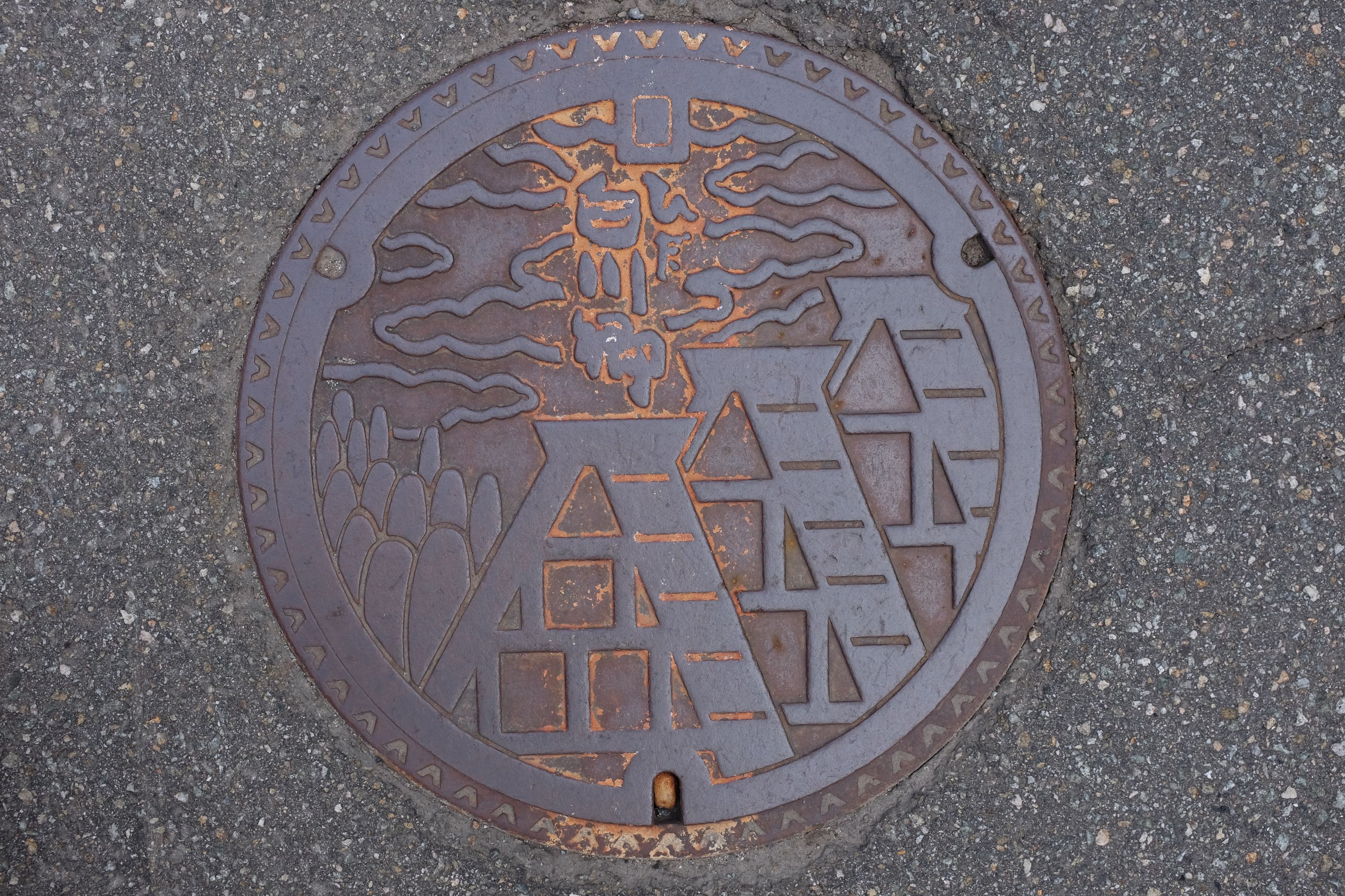 Manhole cover showing a group of thatch-roofed houses.