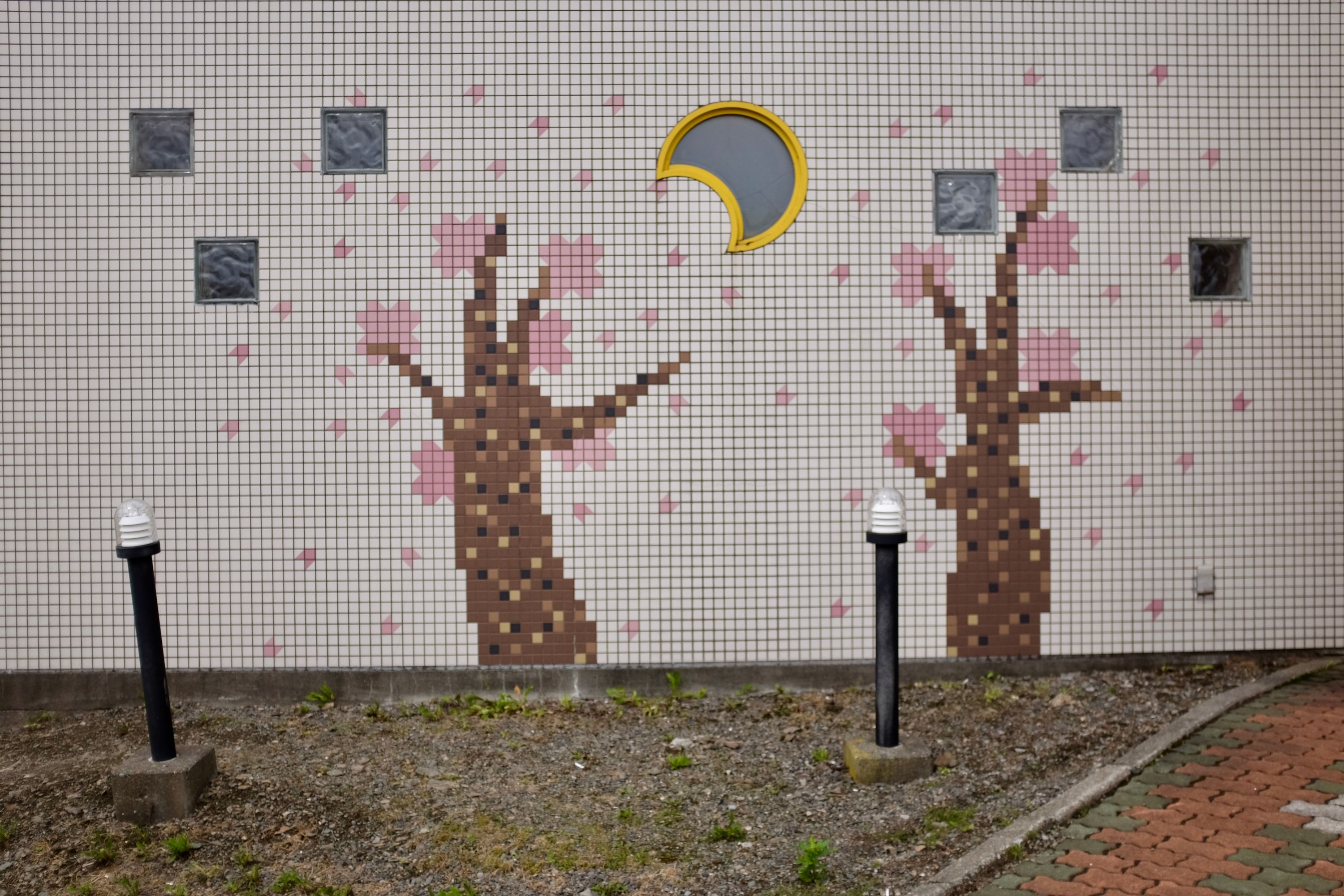 A wall decorated with a mosaic of two trees bearing pink blossom, under a window shaped as a crescent moon.