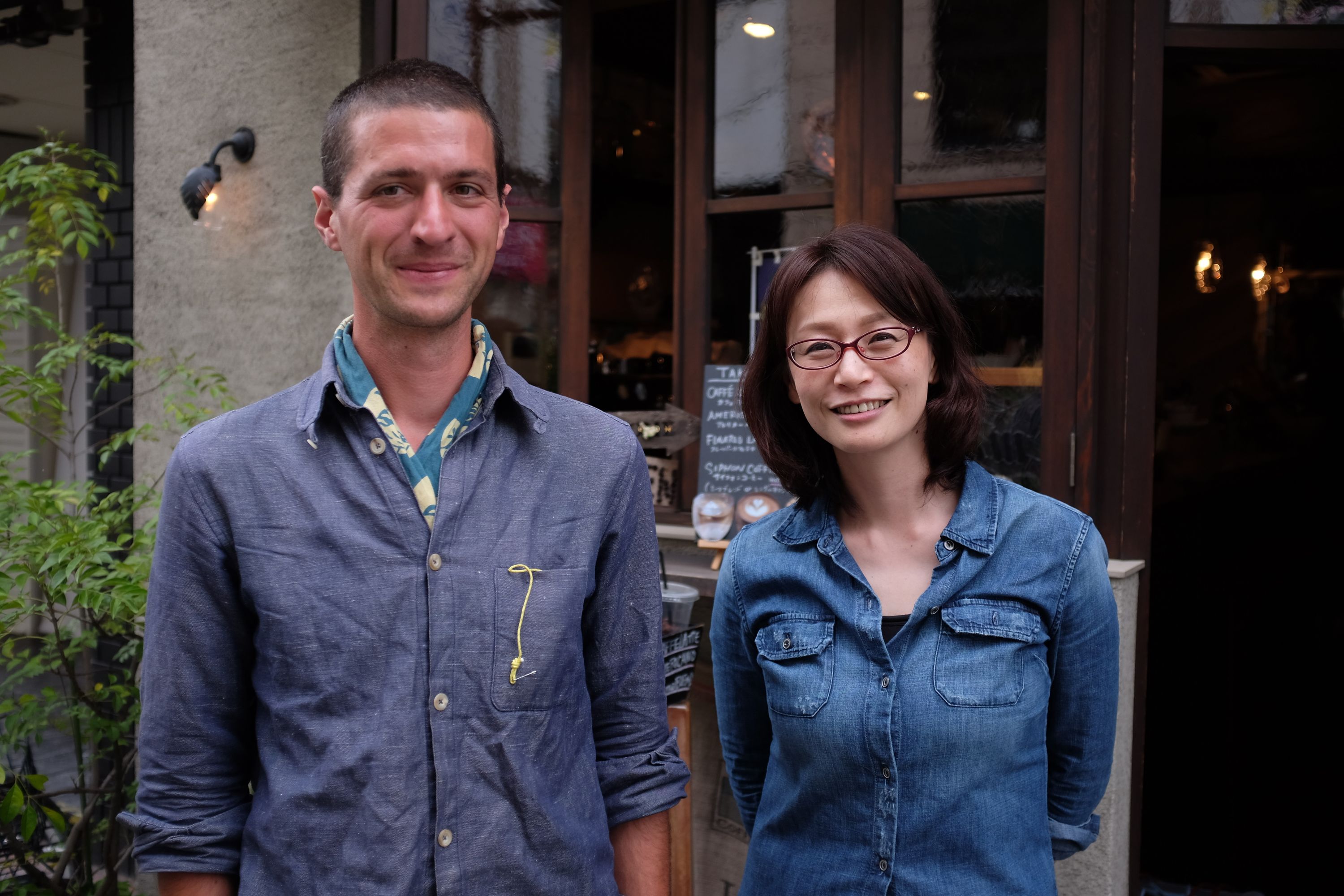 The author, smiling and suntanned, stands in front of a café with Ōhashi Aki, a Japanese woman.