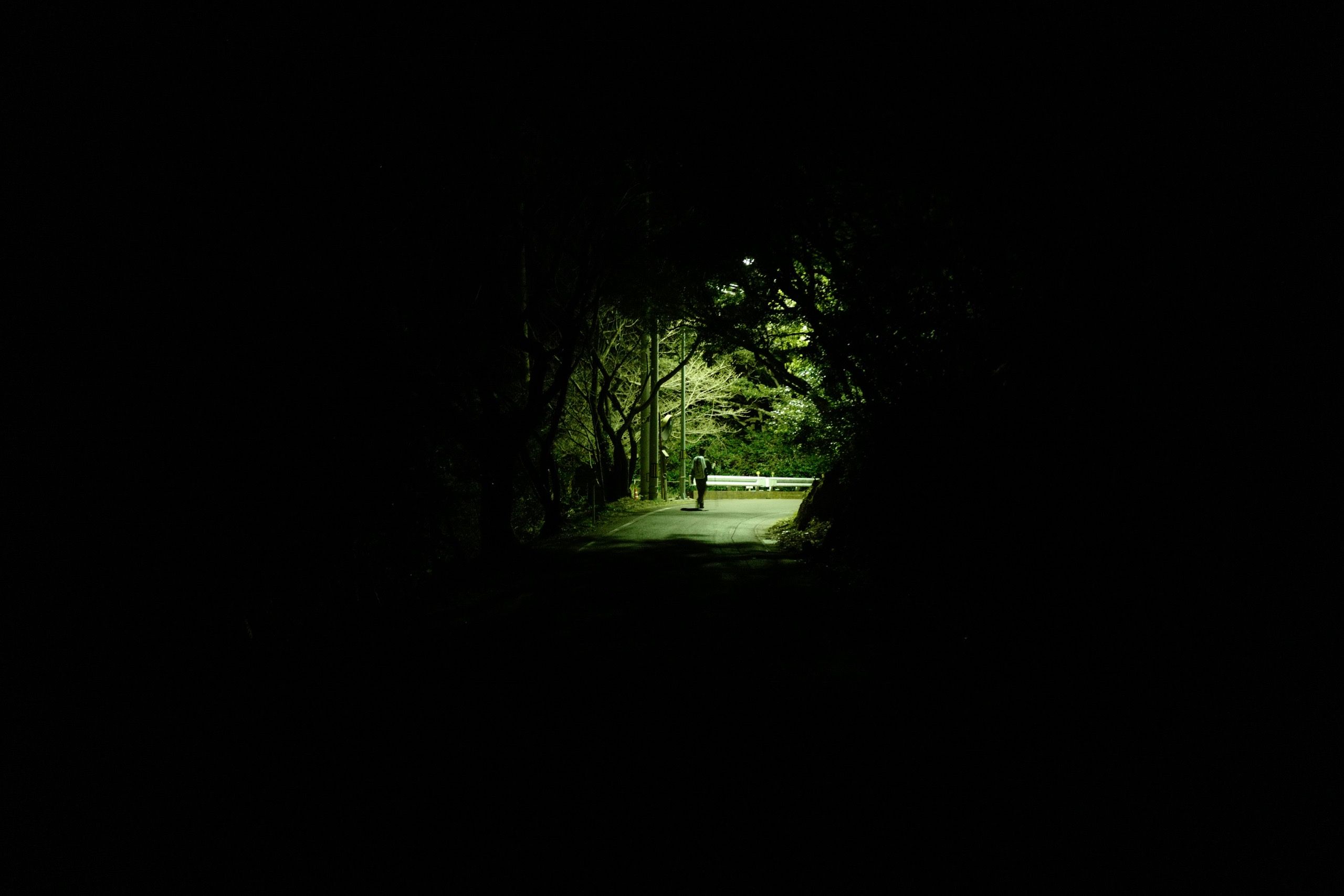 A man carrying a rucksack walks on a road in the distance at night