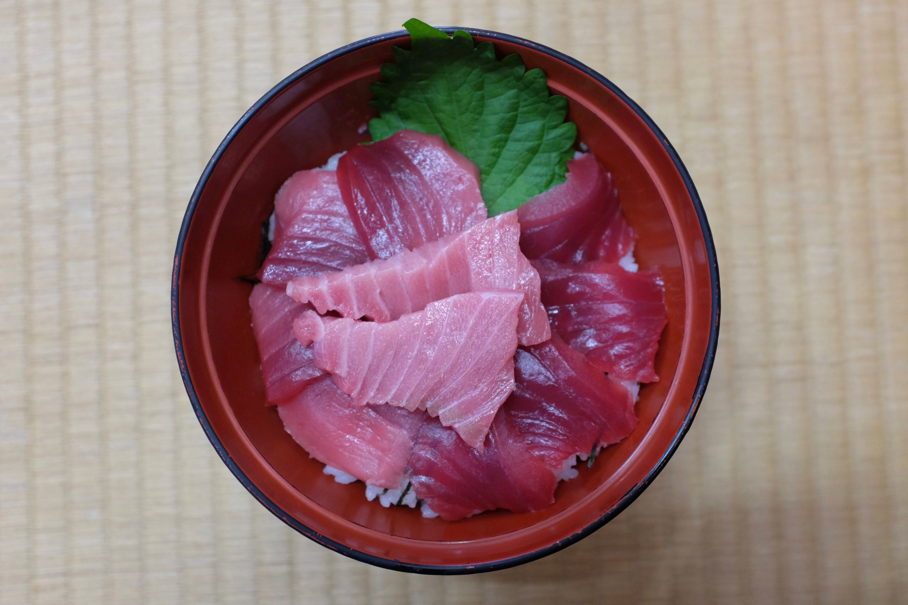 Slices of raw bluefin tuna in a red lacquer bowl, with the different cuts of meat clearly distinguishable by color.