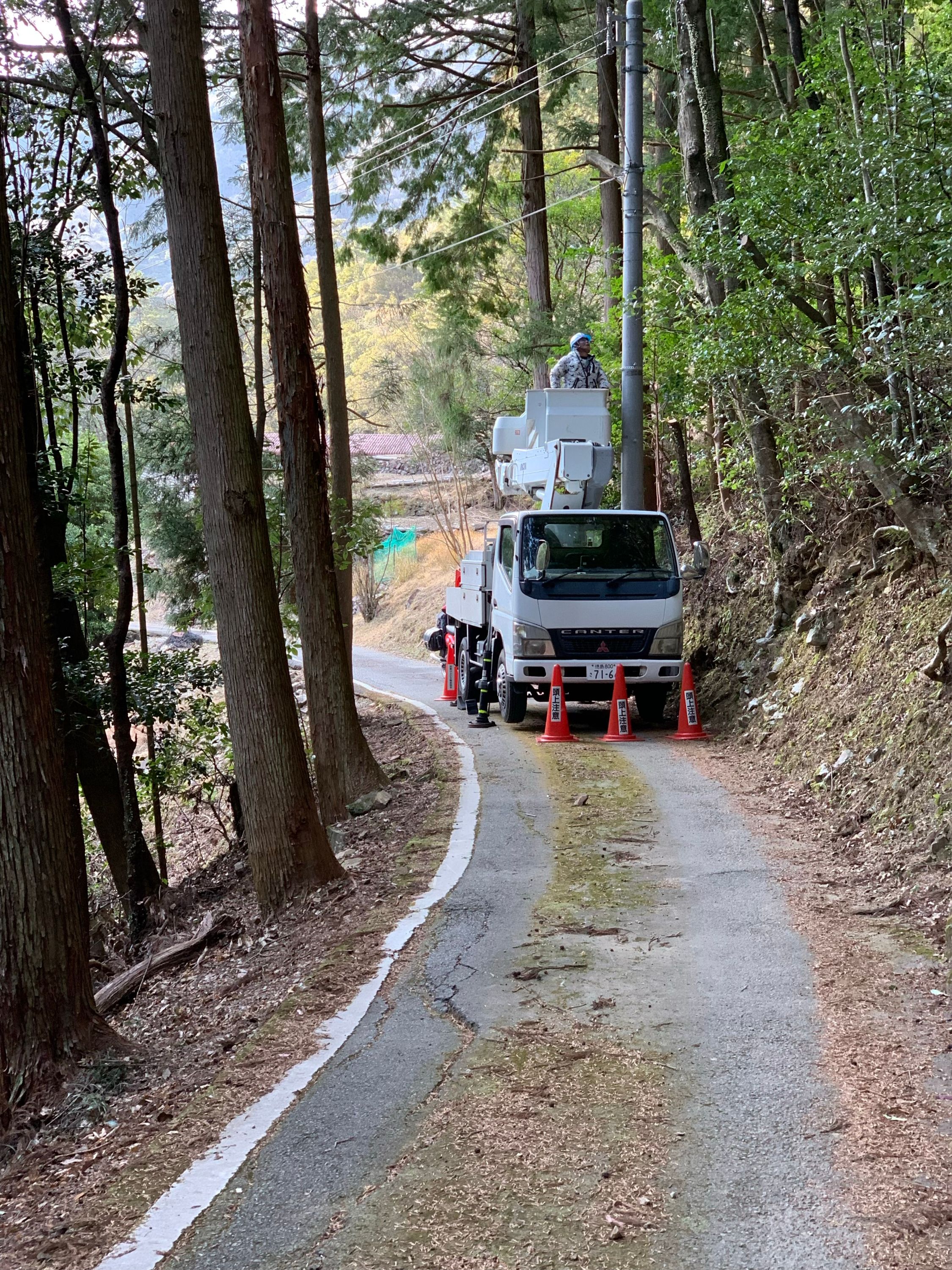 A small truck used by a crew of electricians blocks the entire width of a narrow country road.