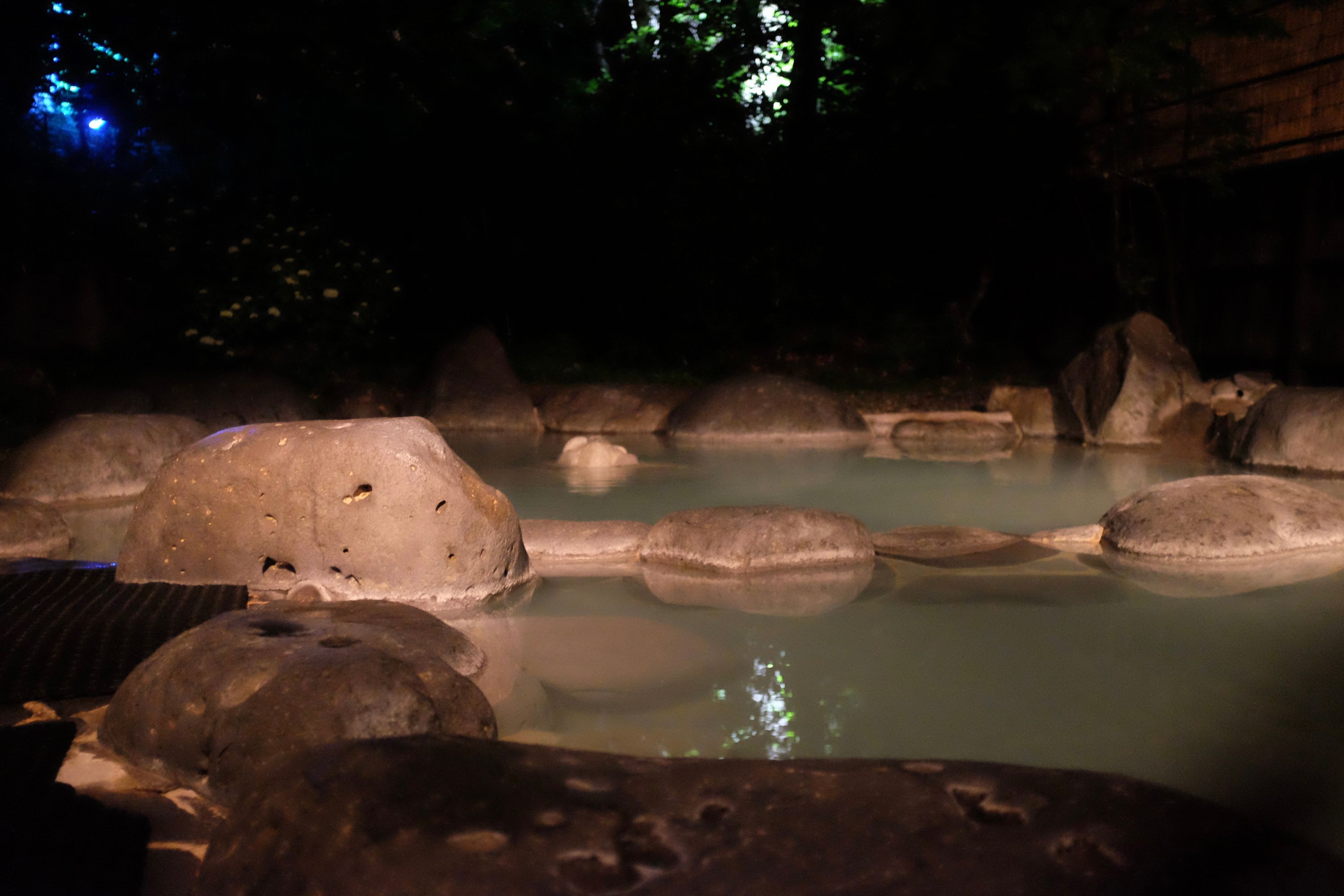 The hazy waters of an outside bath, ringed with large grey stones.