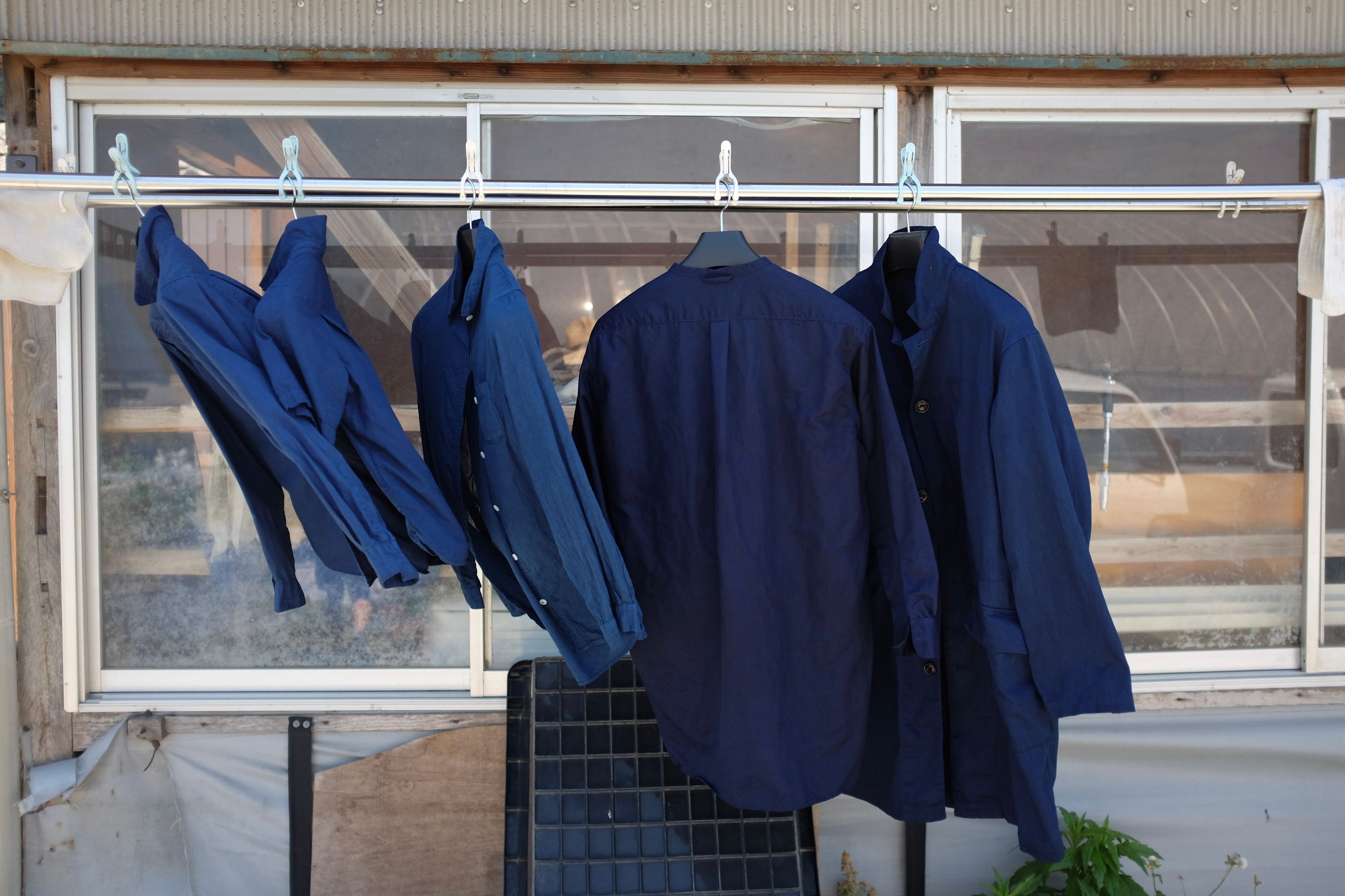 Three shirts and two jackets, all of them dyed indigo, drying in the breeze on a rail.