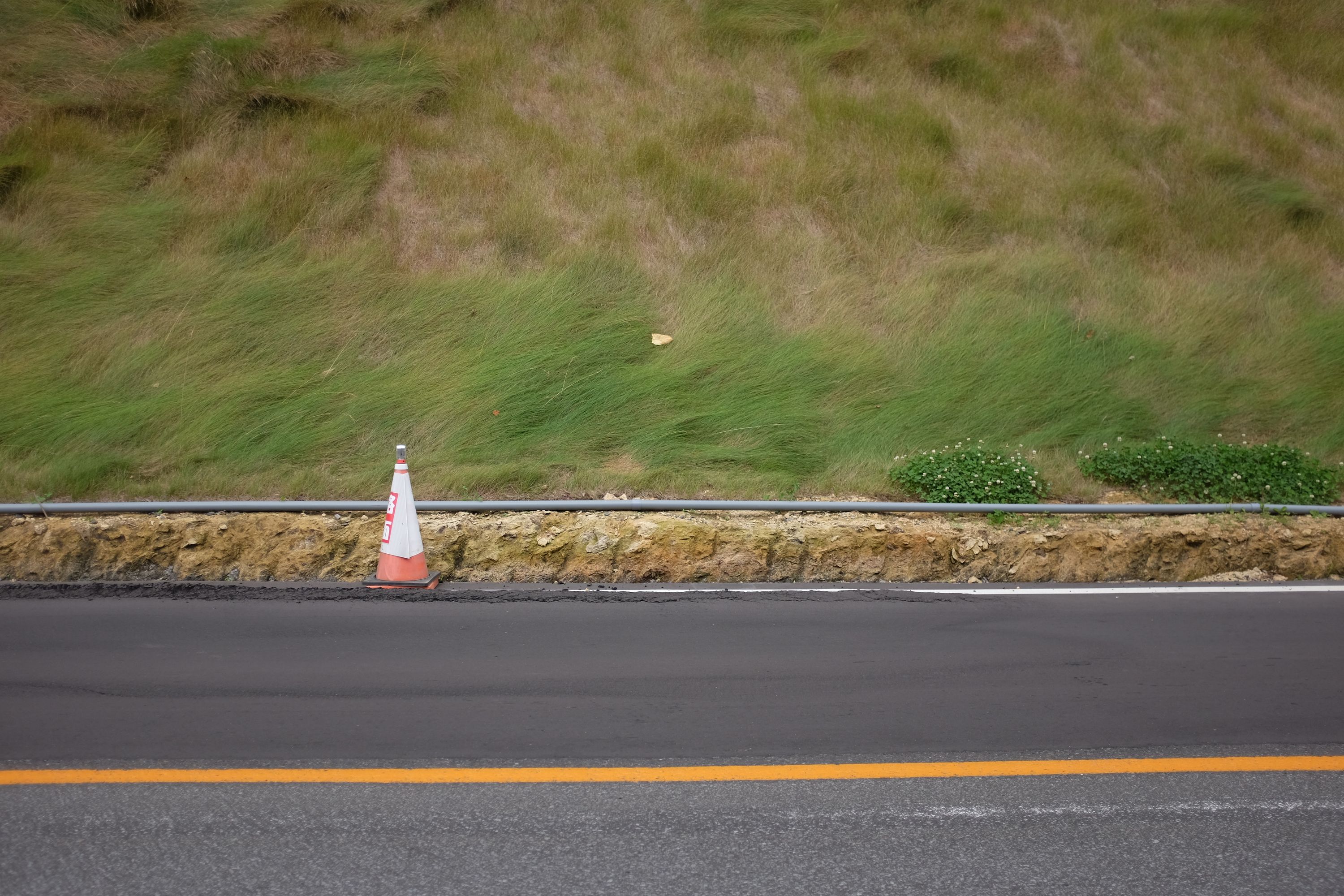 Newly laid asphalt by a hillside covered in silken-looking grass.