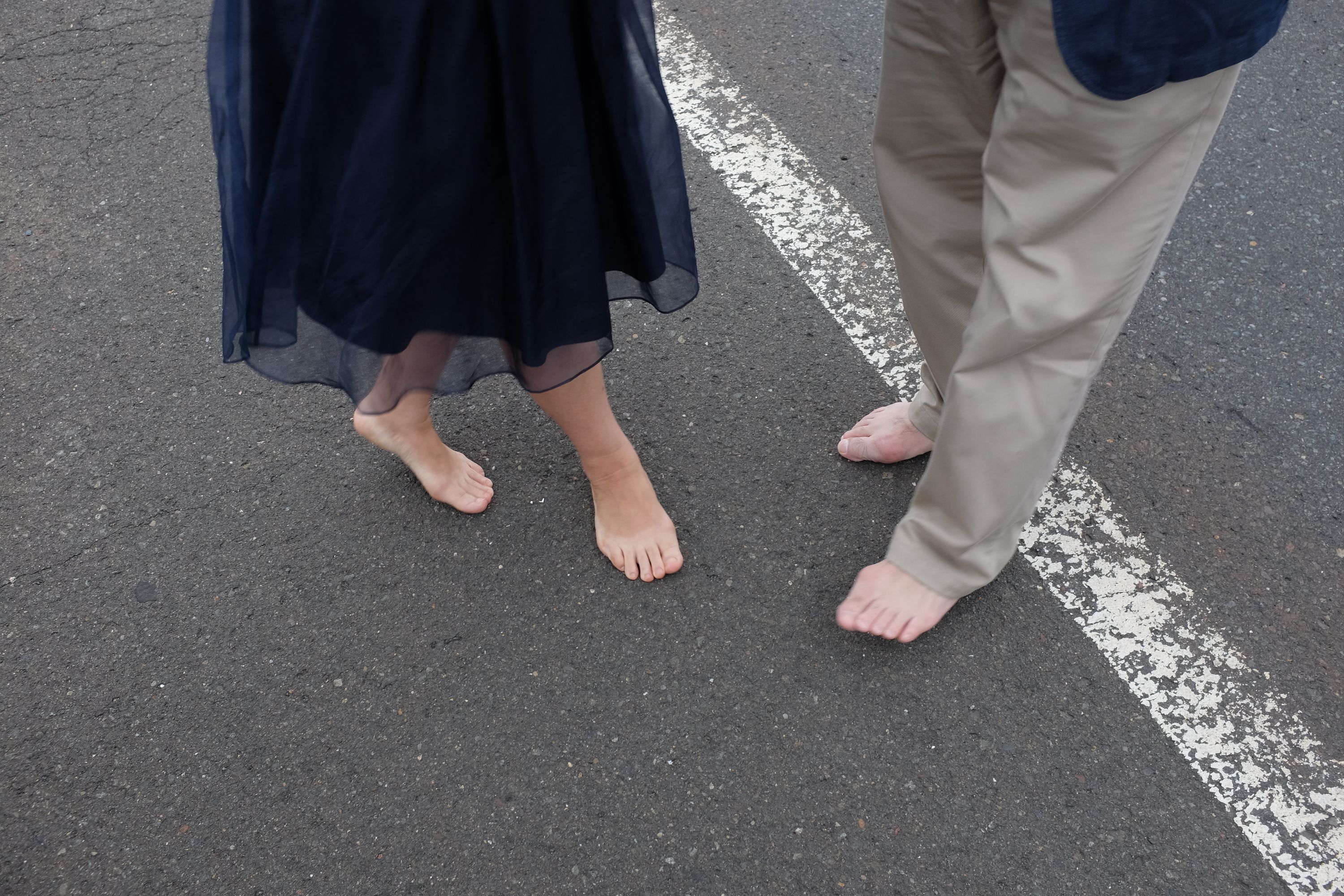 A barefoot couple stand on the asphalt, visible from the waist down.