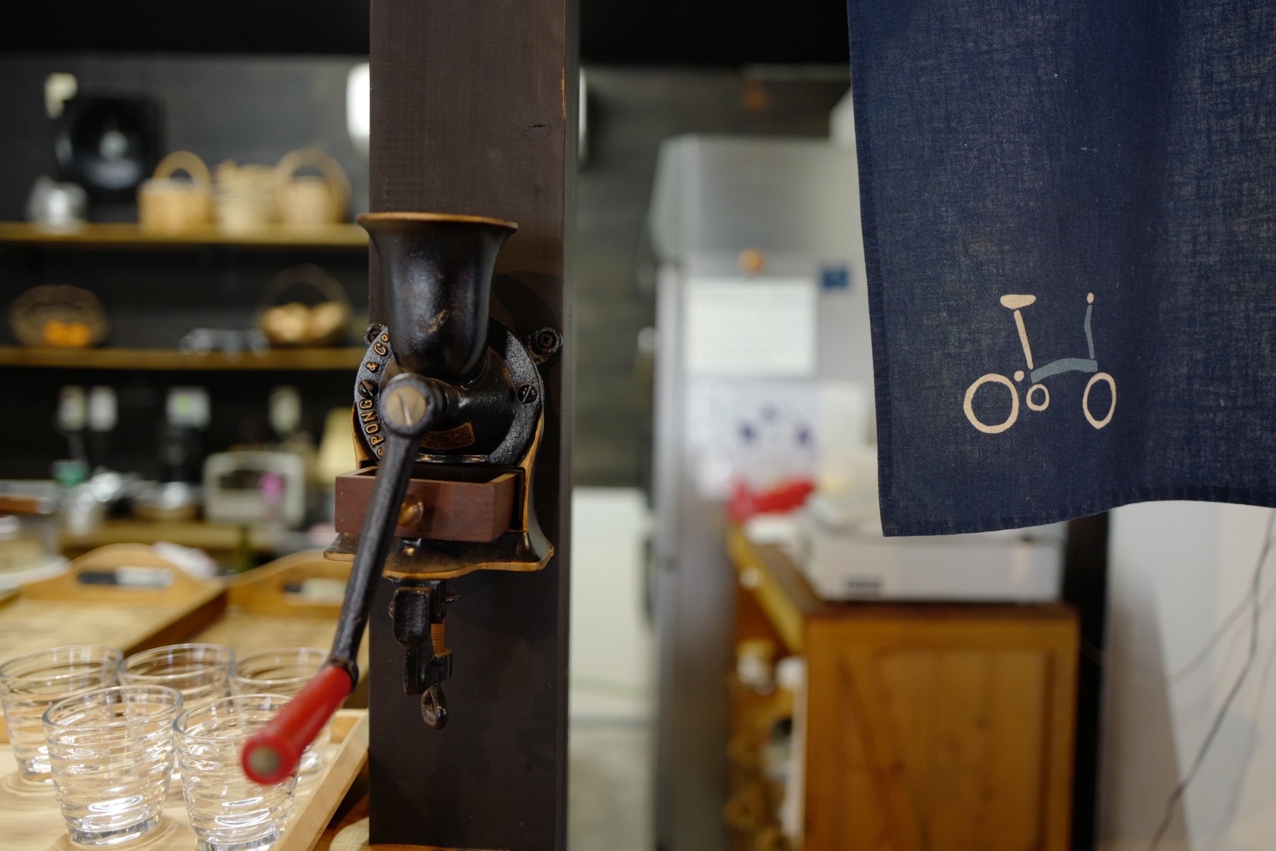 An old coffee grinder and a cloth curtain printed with the silhouette of a Brompton folding bicycle inside the cafe.