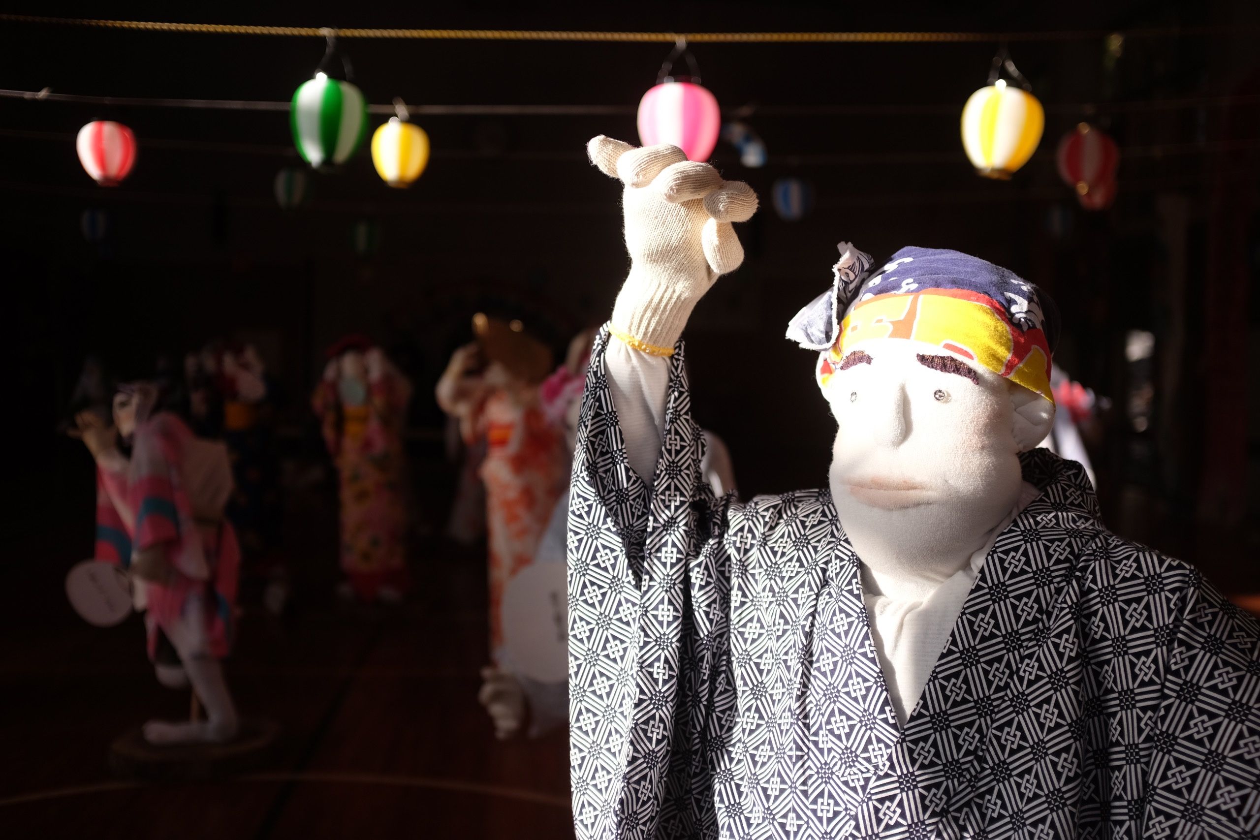Another doll in a Japanese summer kimono stands in a gymnasium, with other dolls in the background.
