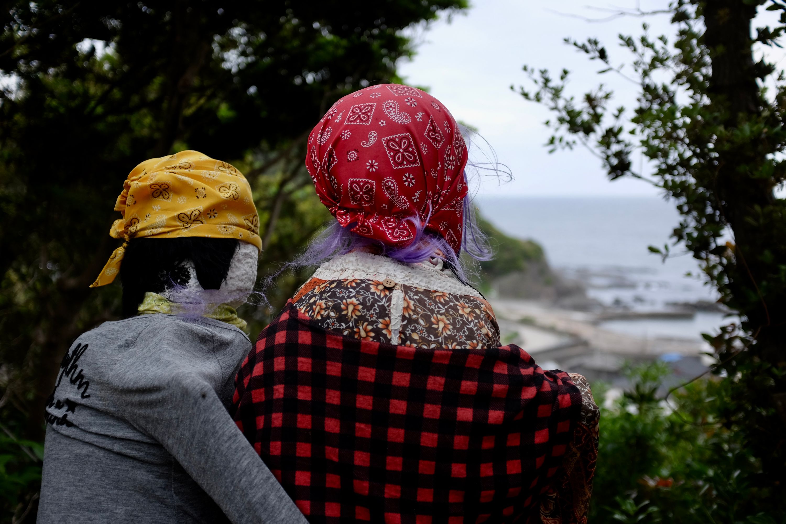 Two dolls in colorful bandannas look out on a small fishing village below them.