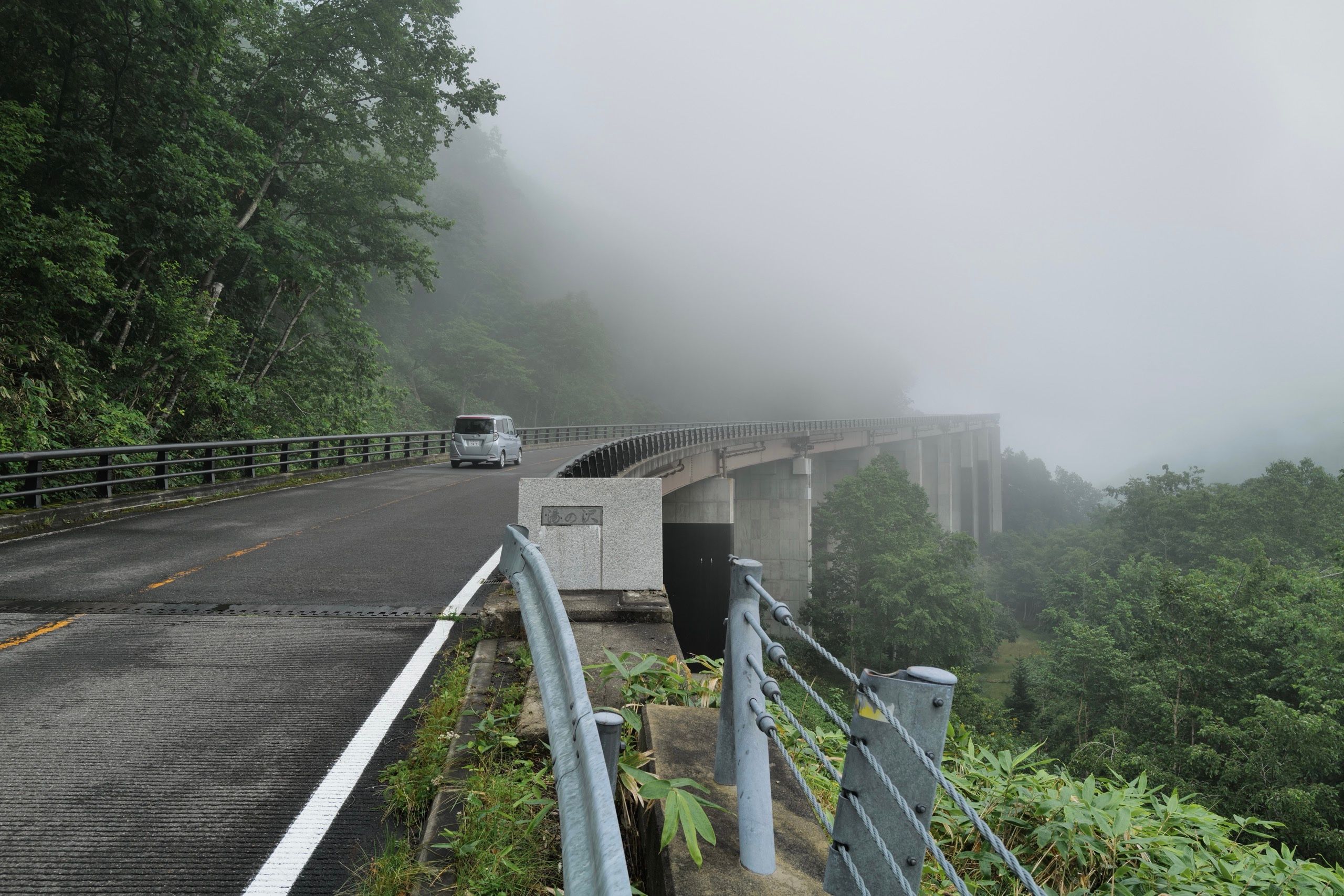 A bridge on a mountain road disappears into the fog.