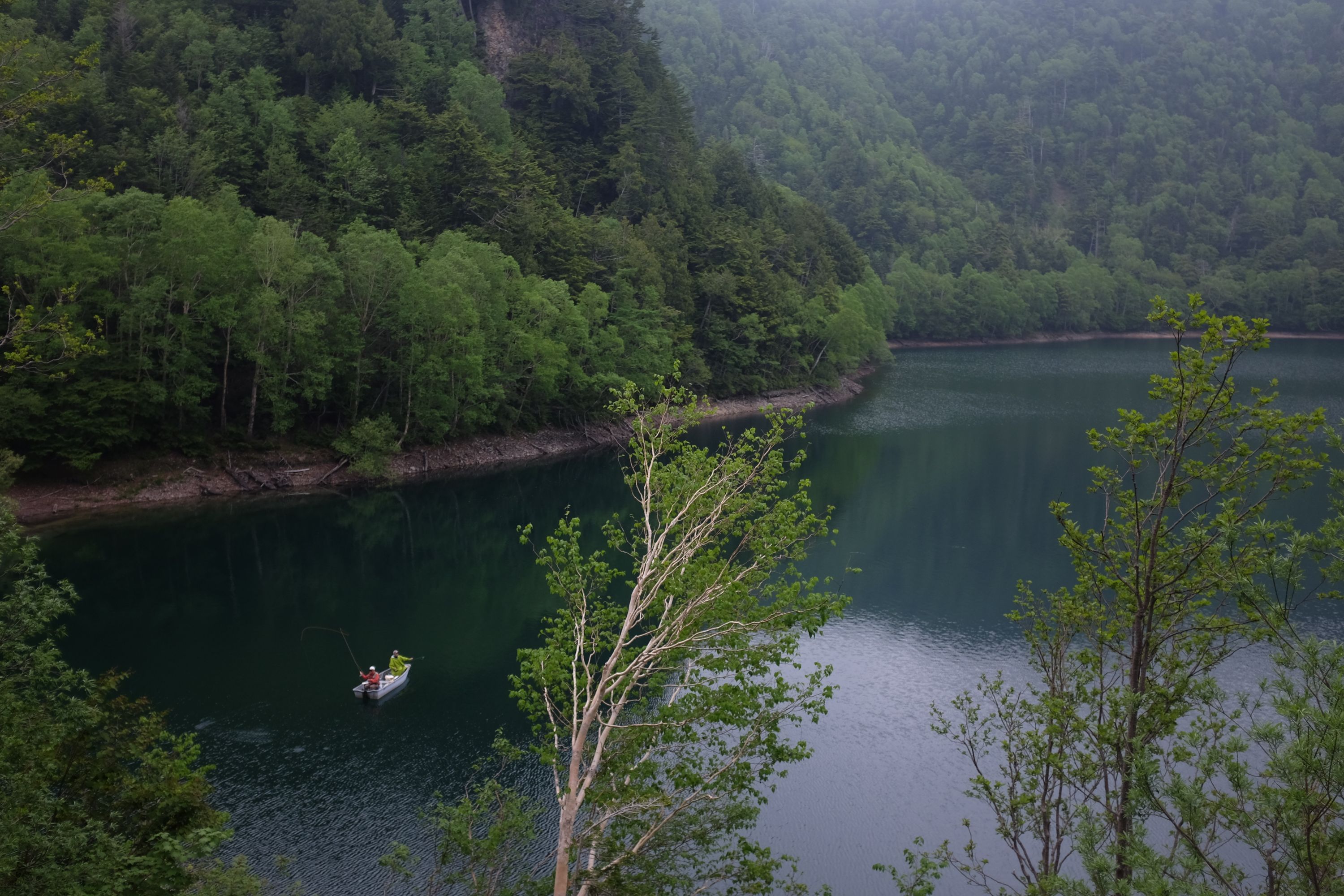 Two men fly-fishing in a boat on a mountain lake.