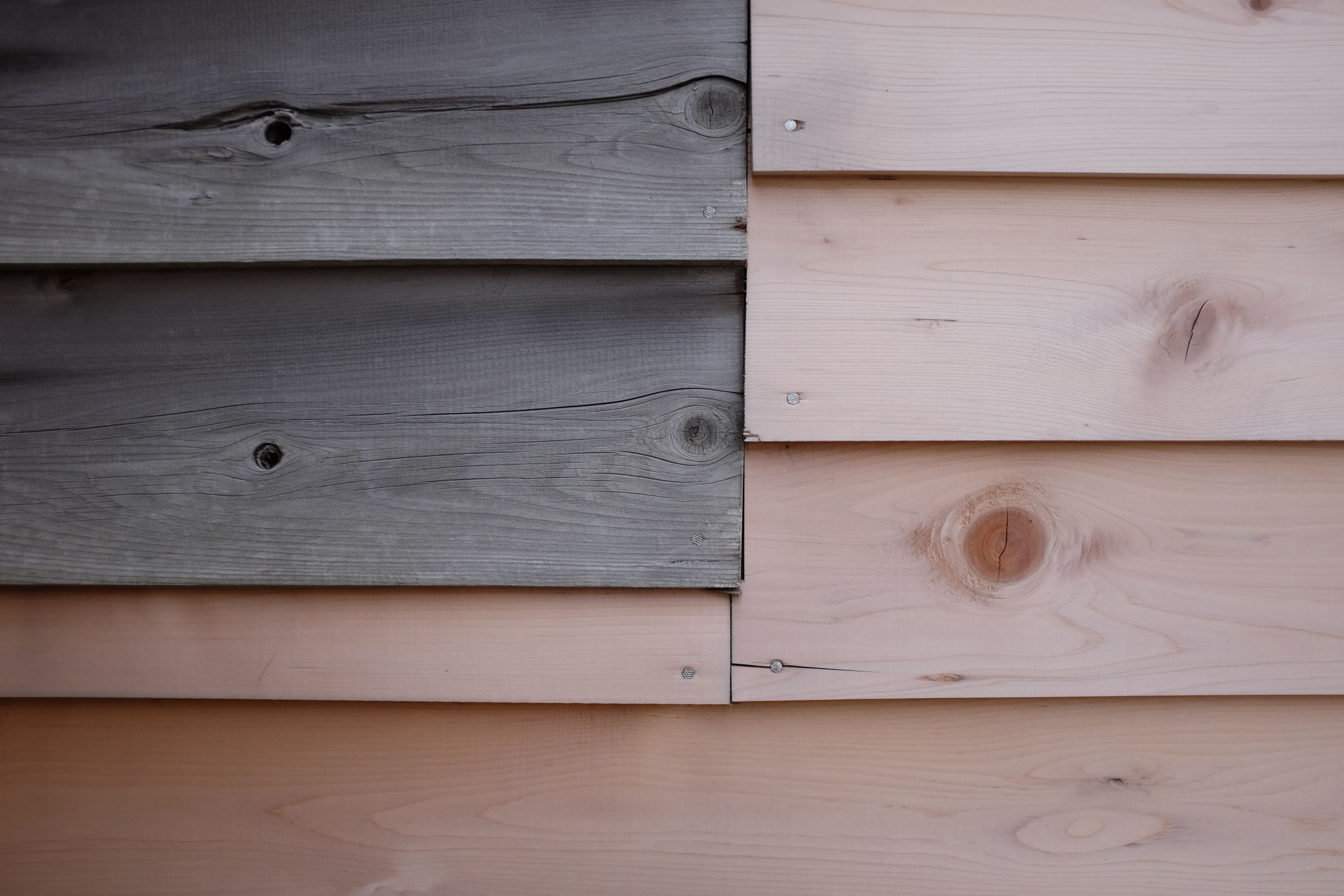 Old and new boards join on the wall of a wooden shack.