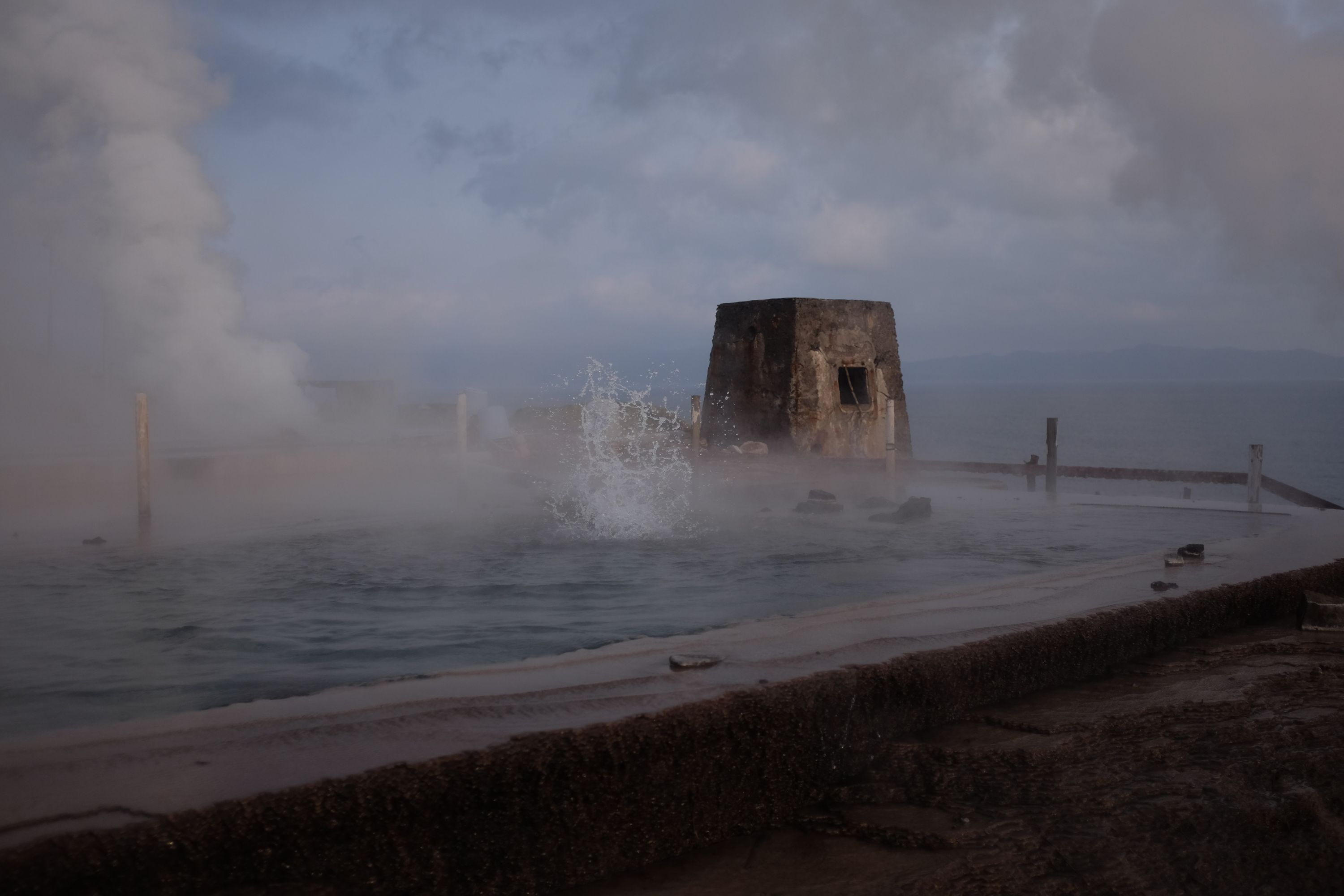 Angry, sputtering hot water in a pool, with the sea visible behind it.