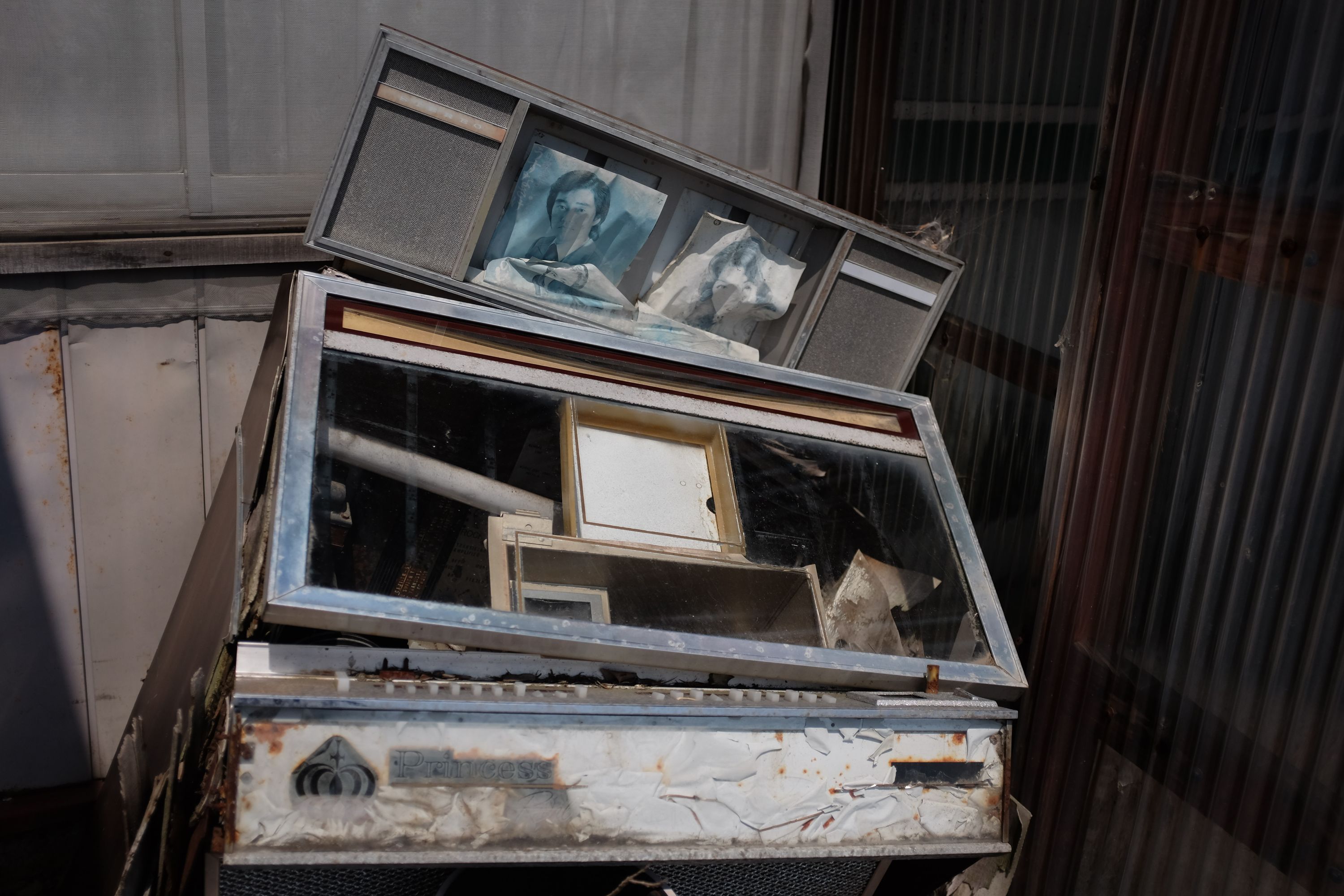 Some sort of discarded appliance with two faded and crumpled pictures of old-fashioned celebrities stuck to it.