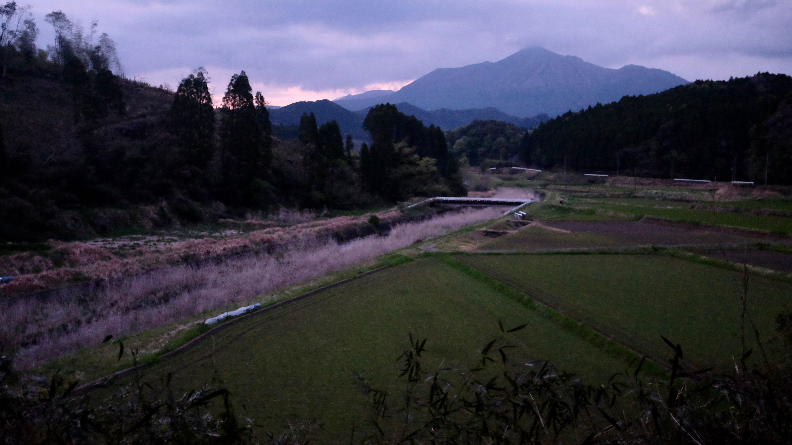 A closer view of the volcano Takachino-no-mine across some fields in the evening light.