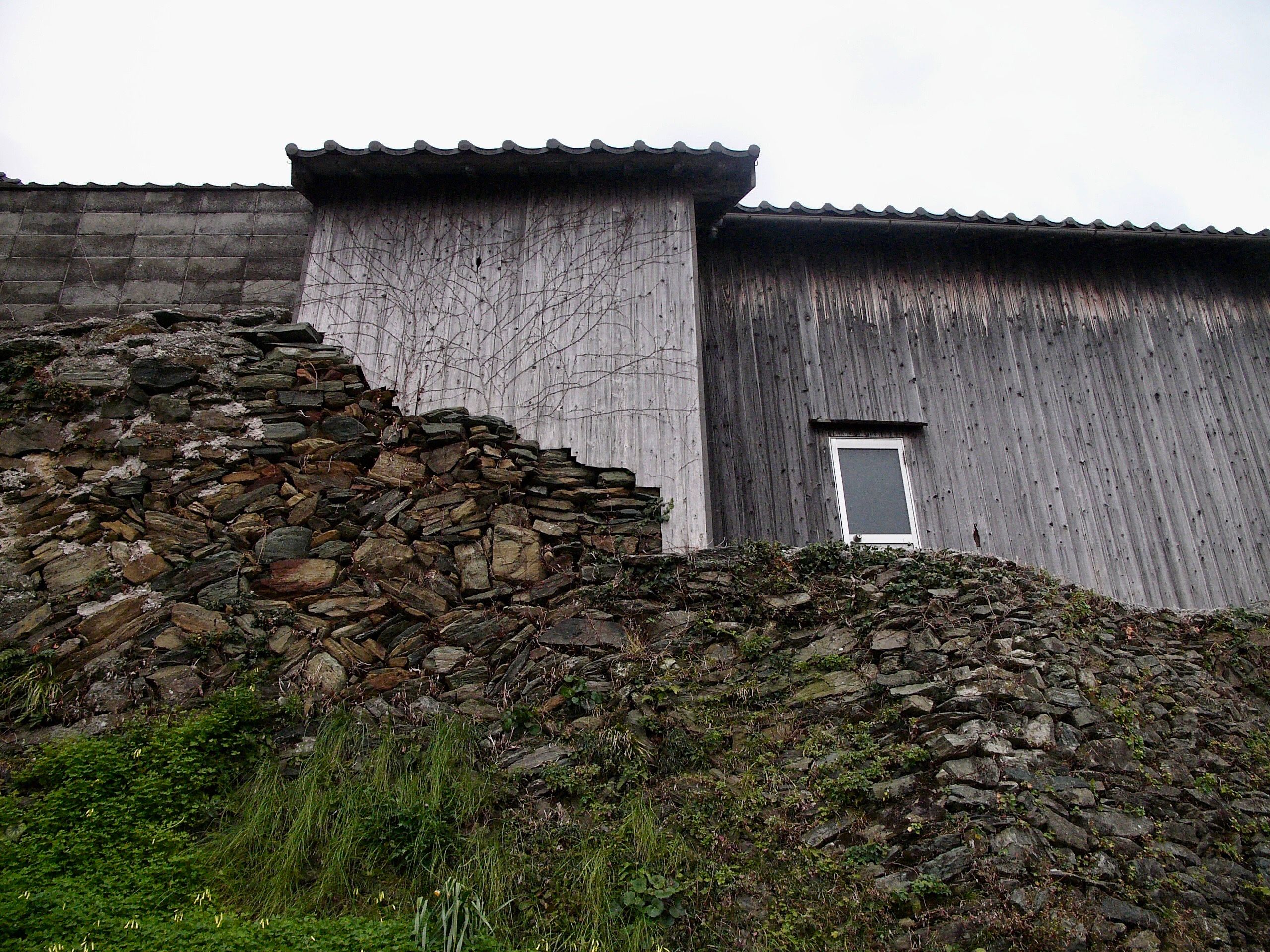 Looking up on a wooden house built atop a stone wall.