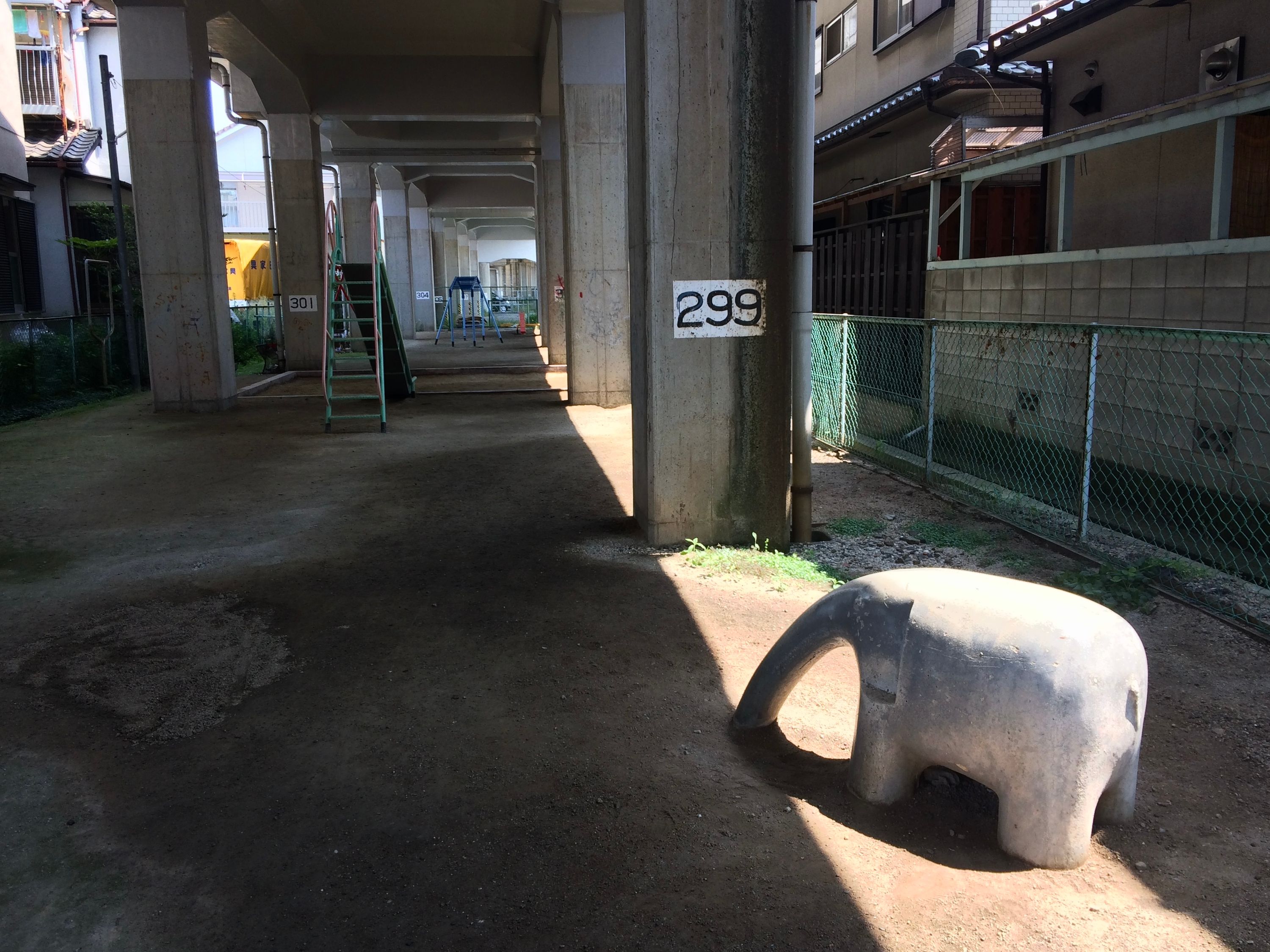 A playground with a slide and a small carved elephant under elevated tracks.