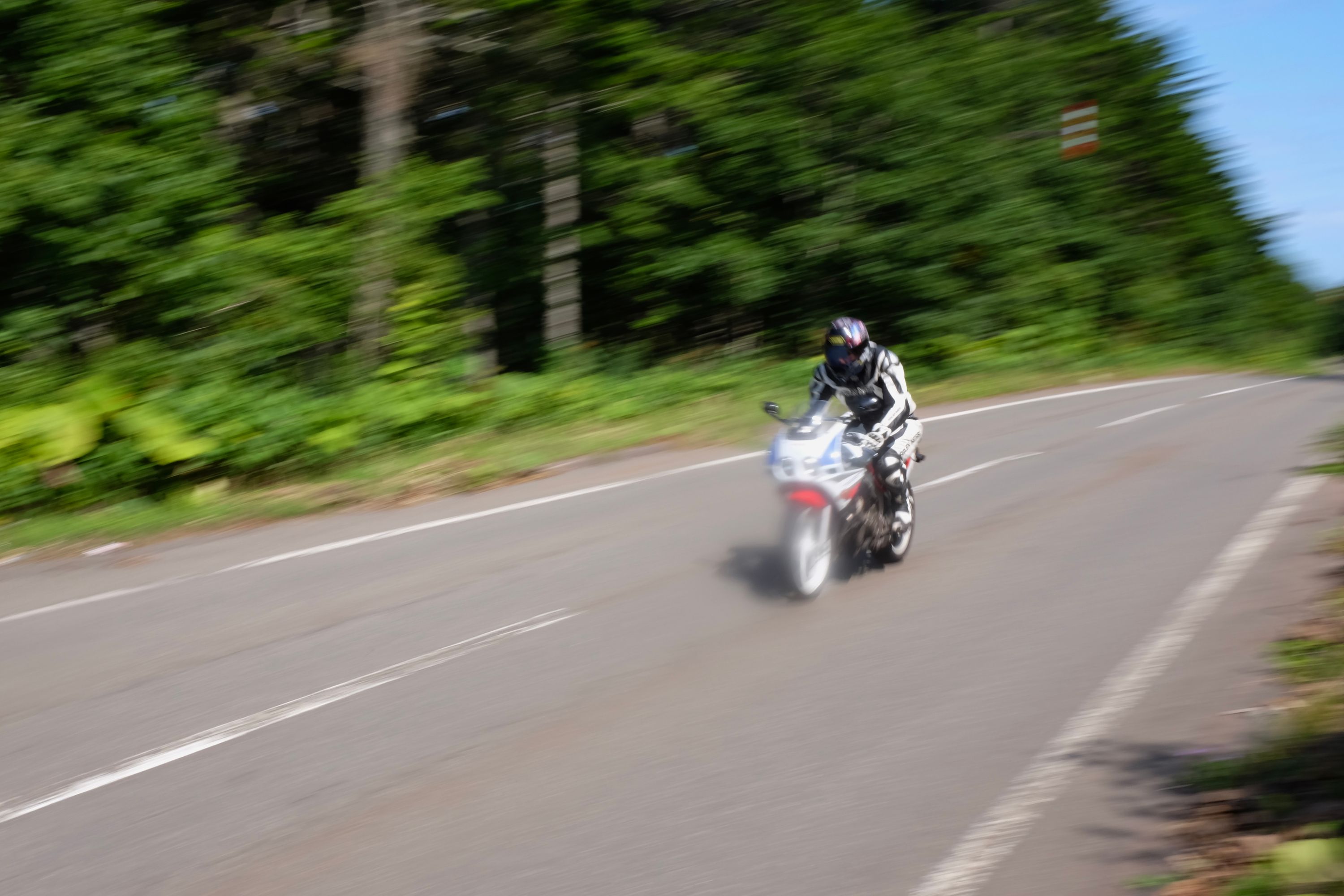 A white motorcycle speeds down a narrow road, its motion blurred.